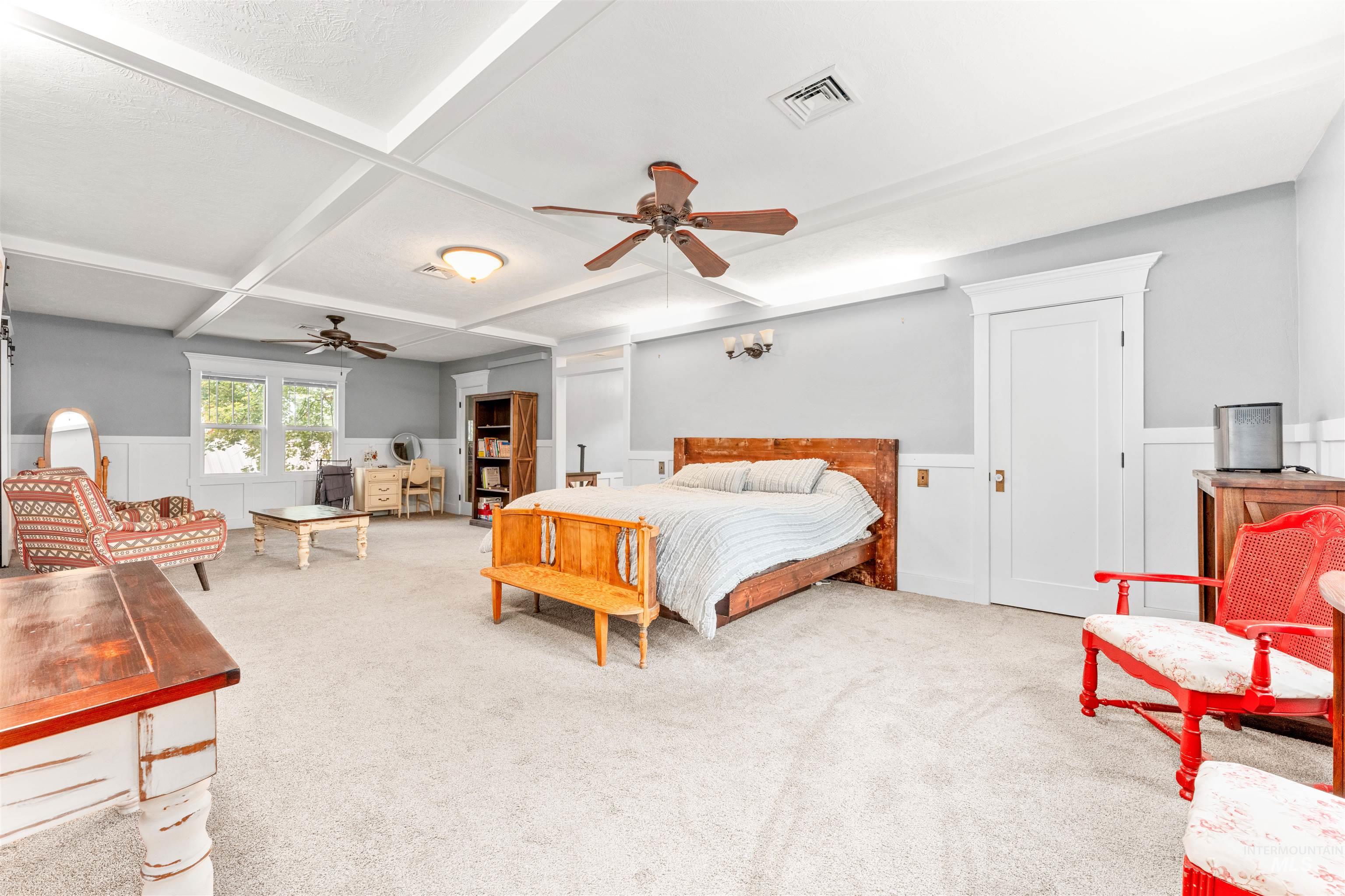 Bedroom featuring wainscoting, coffered ceiling, beam ceiling, carpet, and a decorative wall