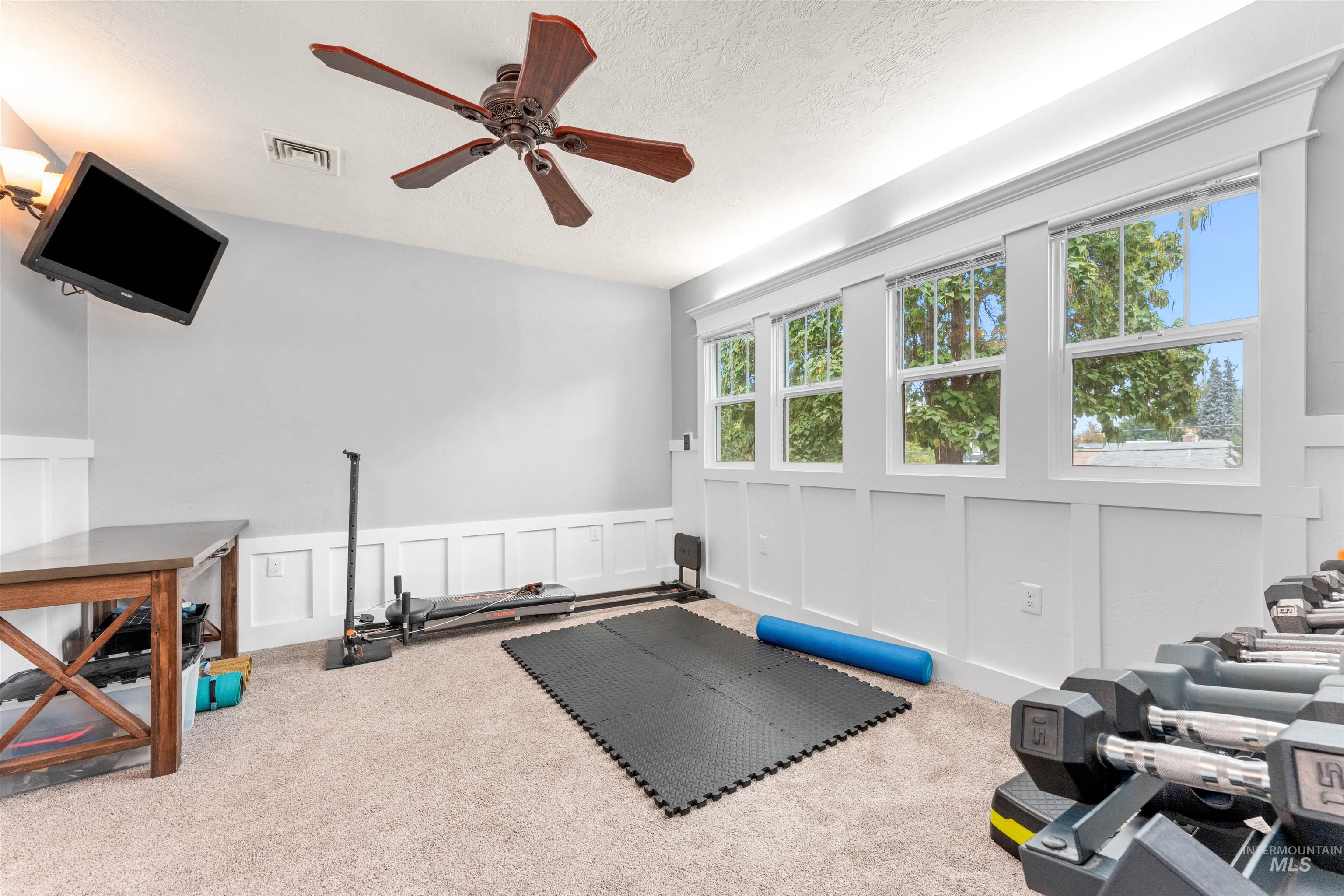 Workout area with a decorative wall, carpet floors, a textured ceiling, wainscoting, and a ceiling fan
