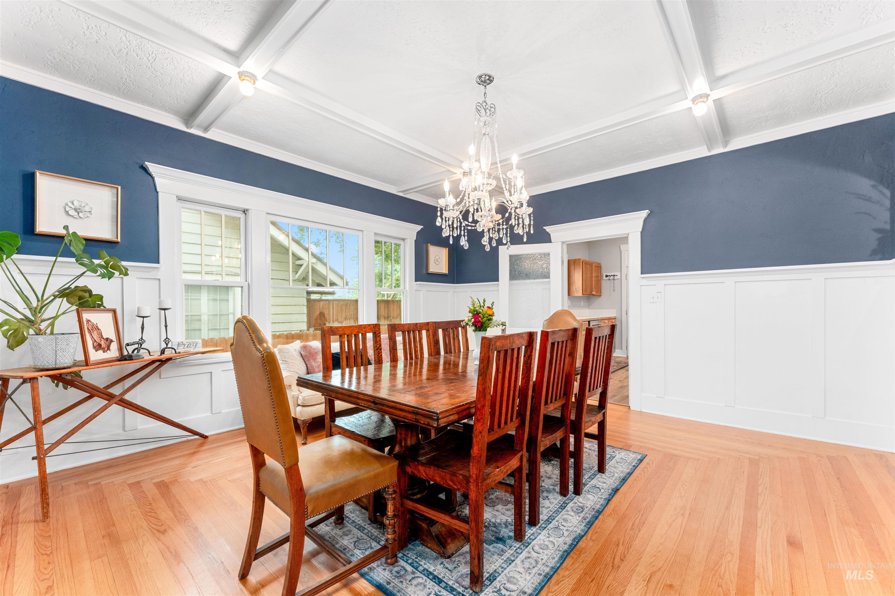 Dining room with a decorative wall, wainscoting, coffered ceiling, a chandelier, and light wood-style flooring