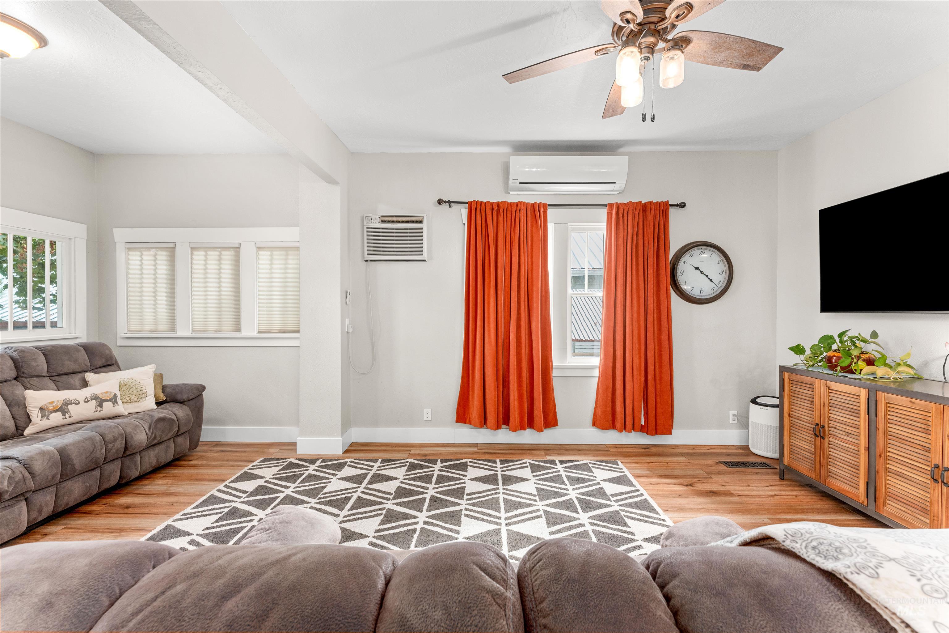 Living area featuring light wood finished floors, a ceiling fan, a wall mounted air conditioner, and a wall unit AC
