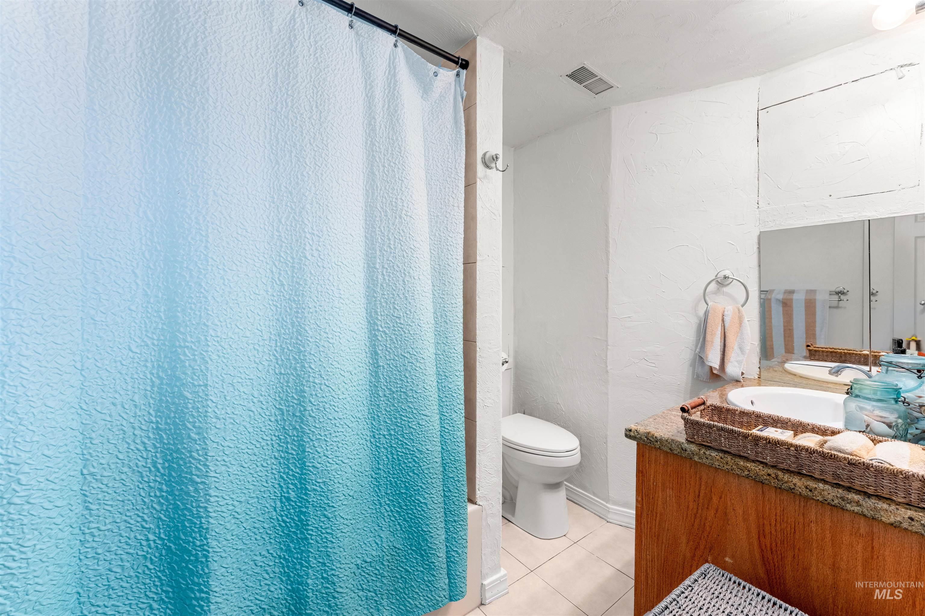 Bathroom featuring a textured wall, vanity, light tile patterned flooring, and a shower with curtain