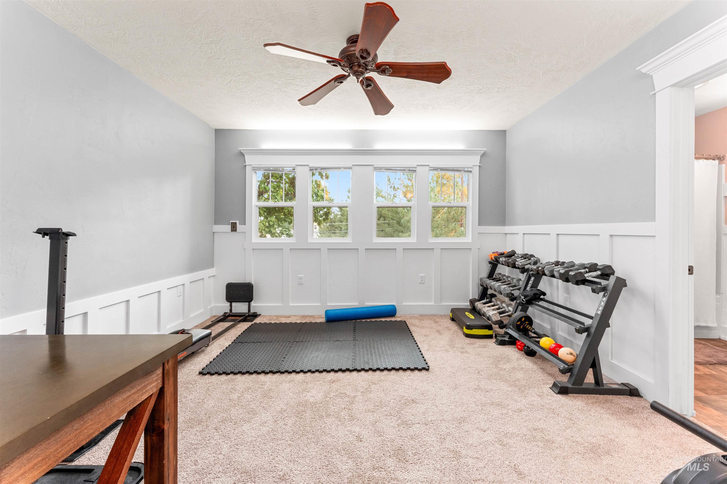 Workout area featuring a decorative wall, a wainscoted wall, ceiling fan, carpet, and a textured ceiling