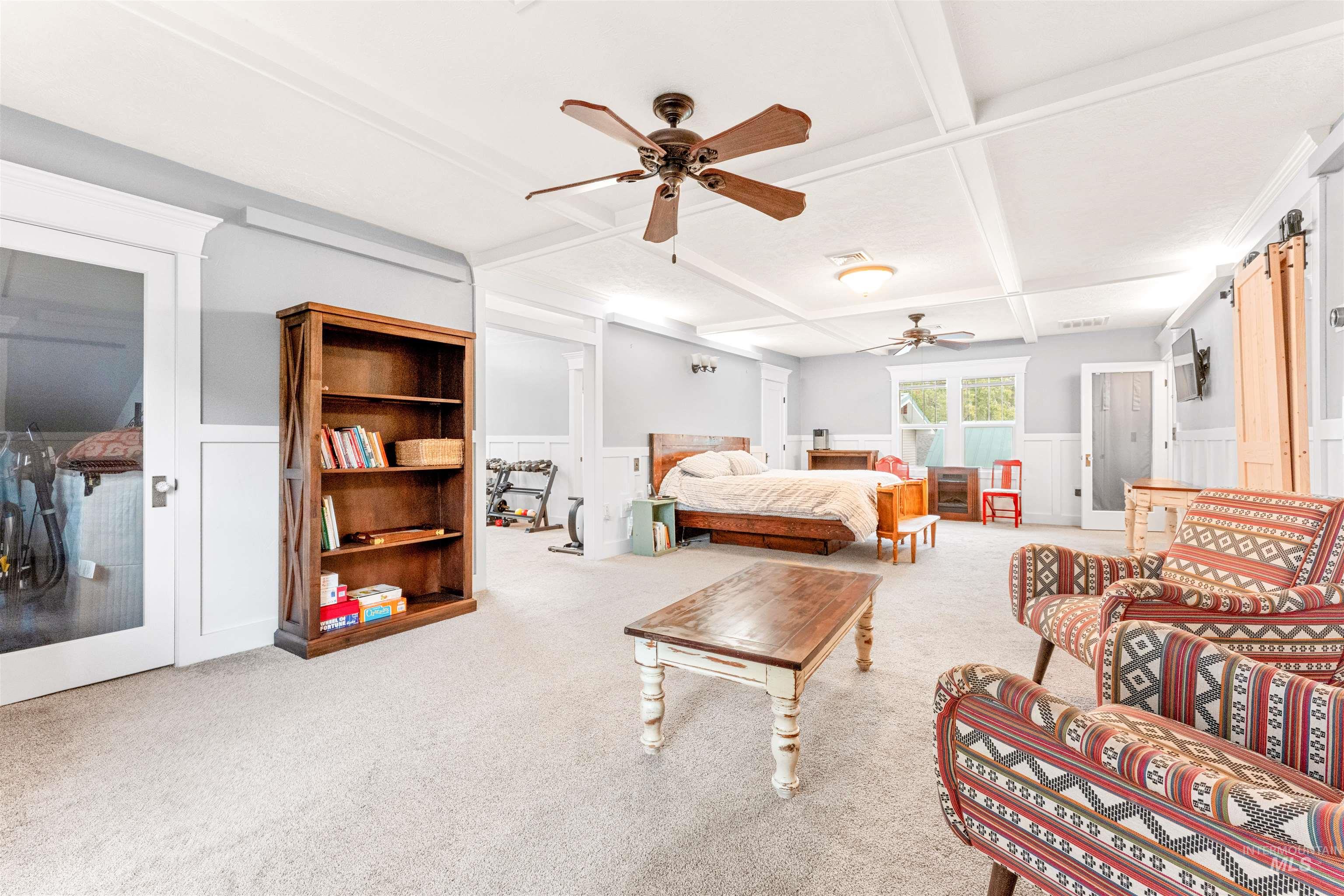 Bedroom featuring beamed ceiling, coffered ceiling, a wainscoted wall, ceiling fan, and carpet flooring