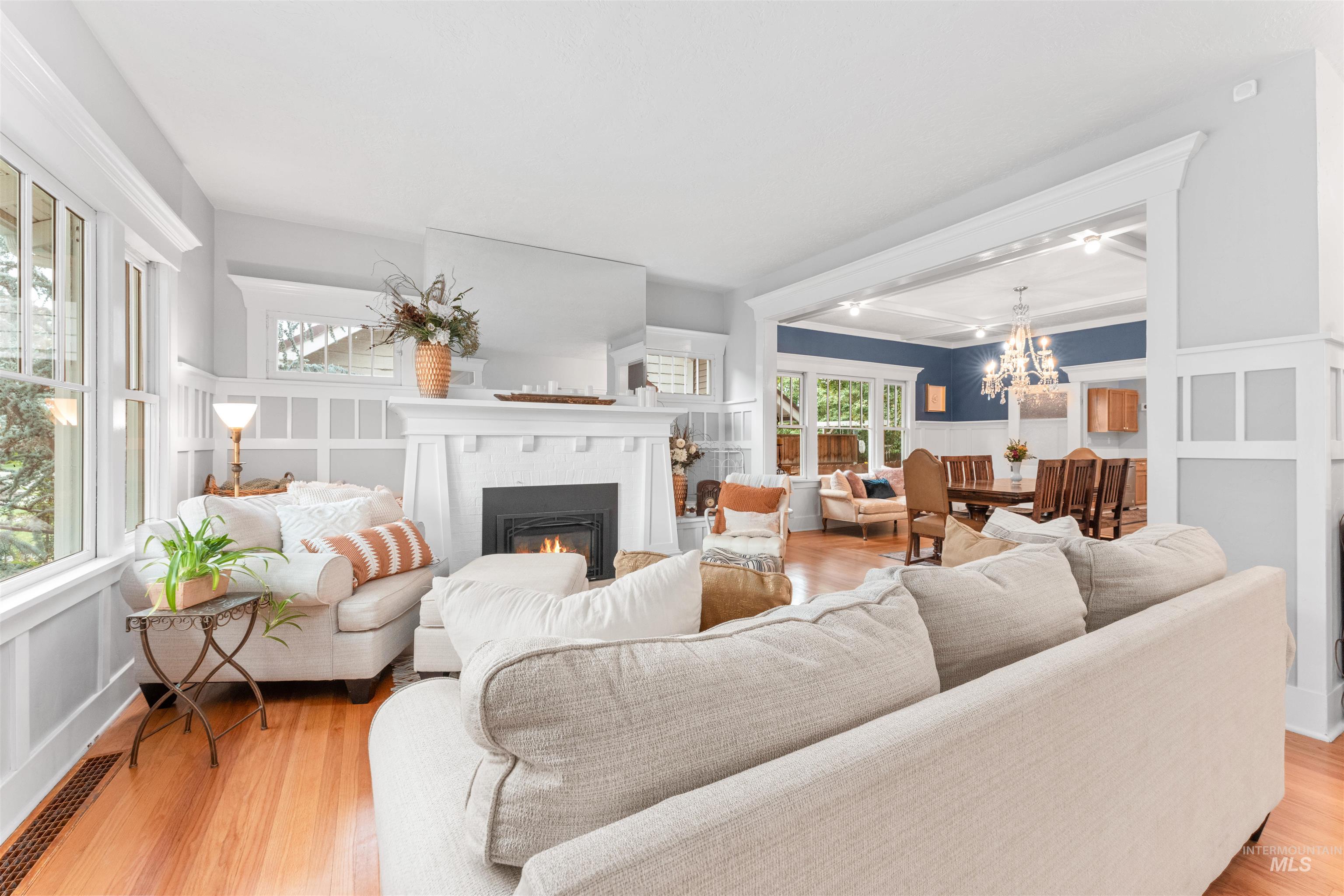 Living area featuring a decorative wall, a warm lit fireplace, wainscoting, light wood-style flooring, and a chandelier