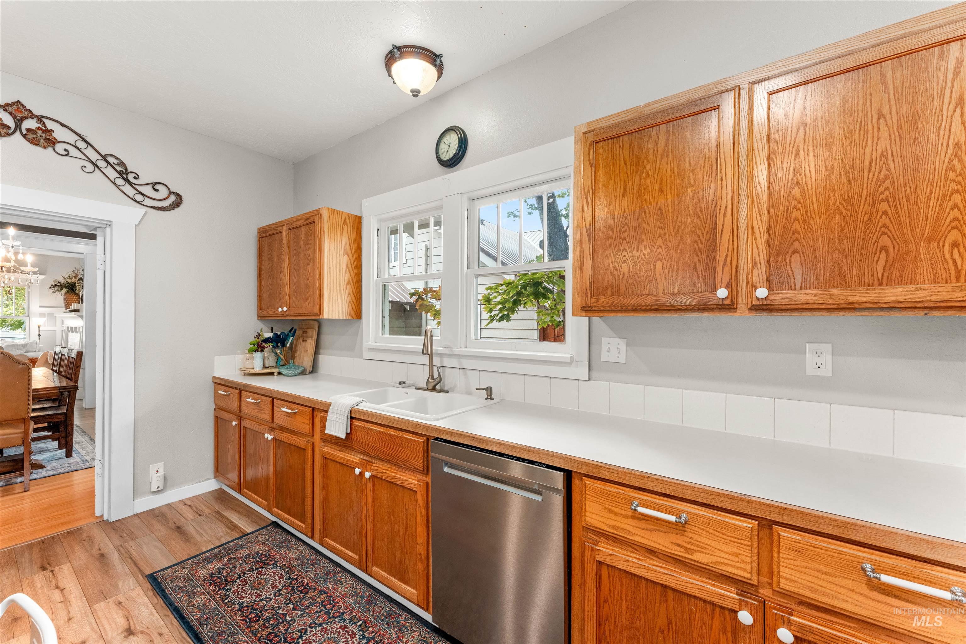 Kitchen with light countertops, dishwasher, brown cabinetry, healthy amount of natural light, and light wood-style floors