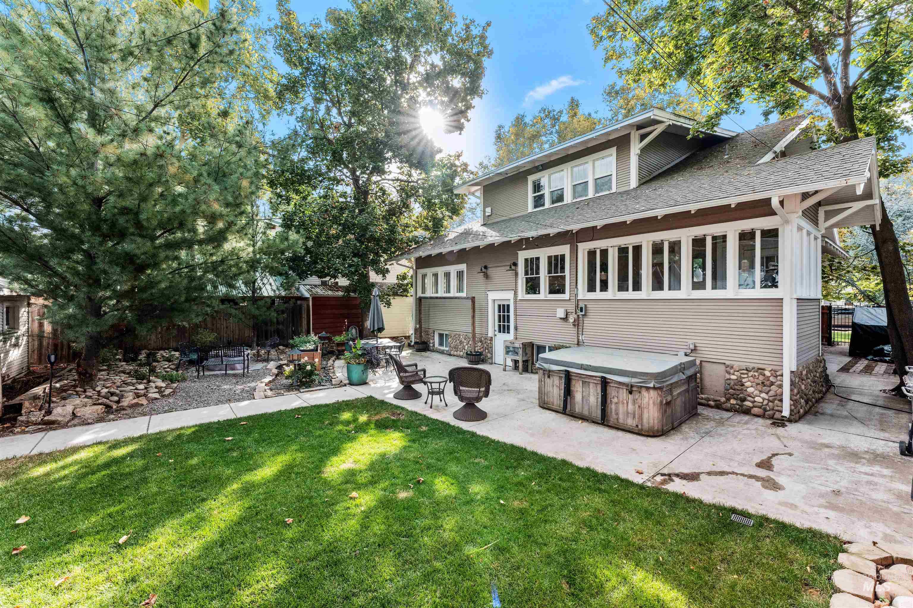 Back of property with a shingled roof, a patio area, a fire pit, a hot tub, and a sunroom