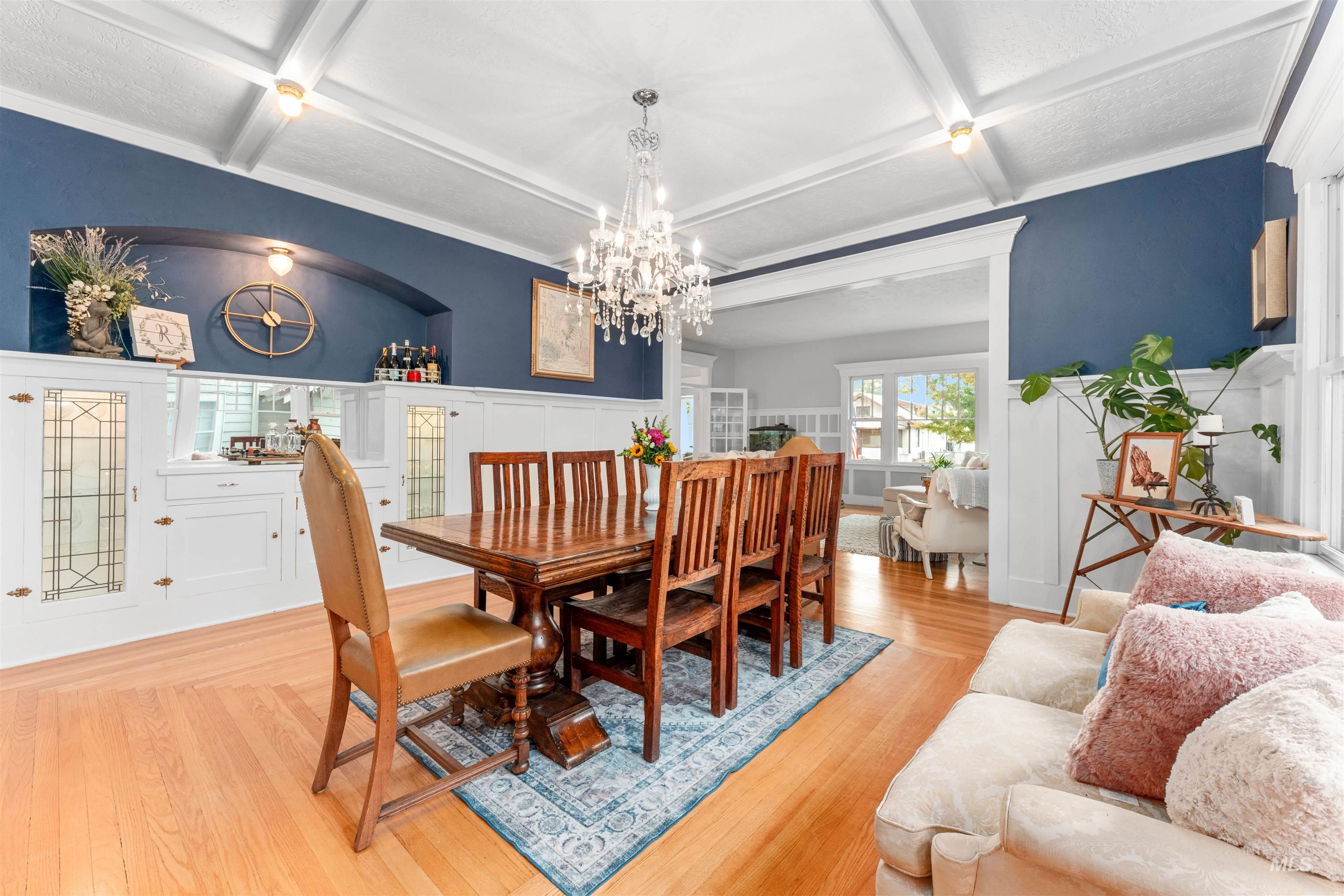 Dining room with coffered ceiling, beamed ceiling, light wood finished floors, a chandelier, and ornamental molding