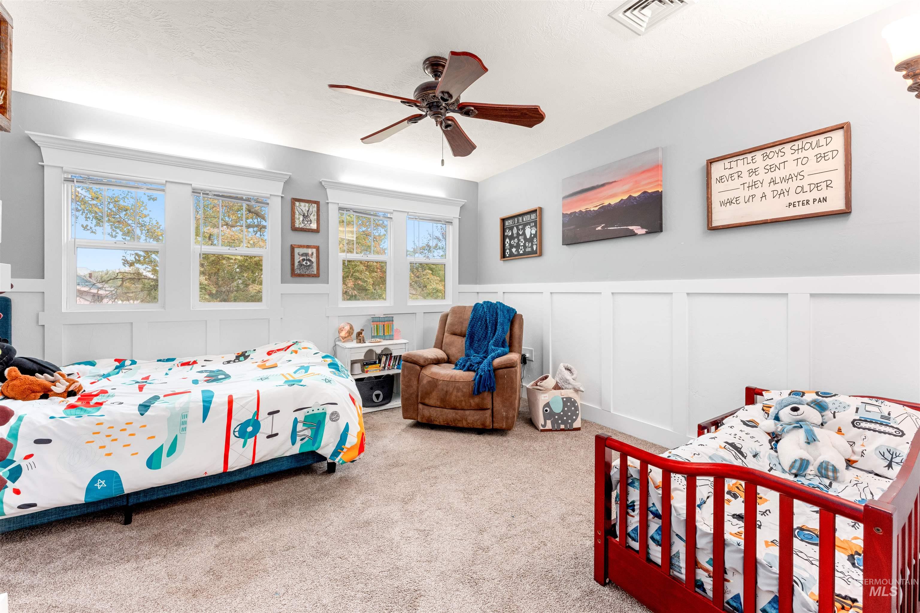 Bedroom with a decorative wall, a wainscoted wall, carpet, ceiling fan, and a textured ceiling