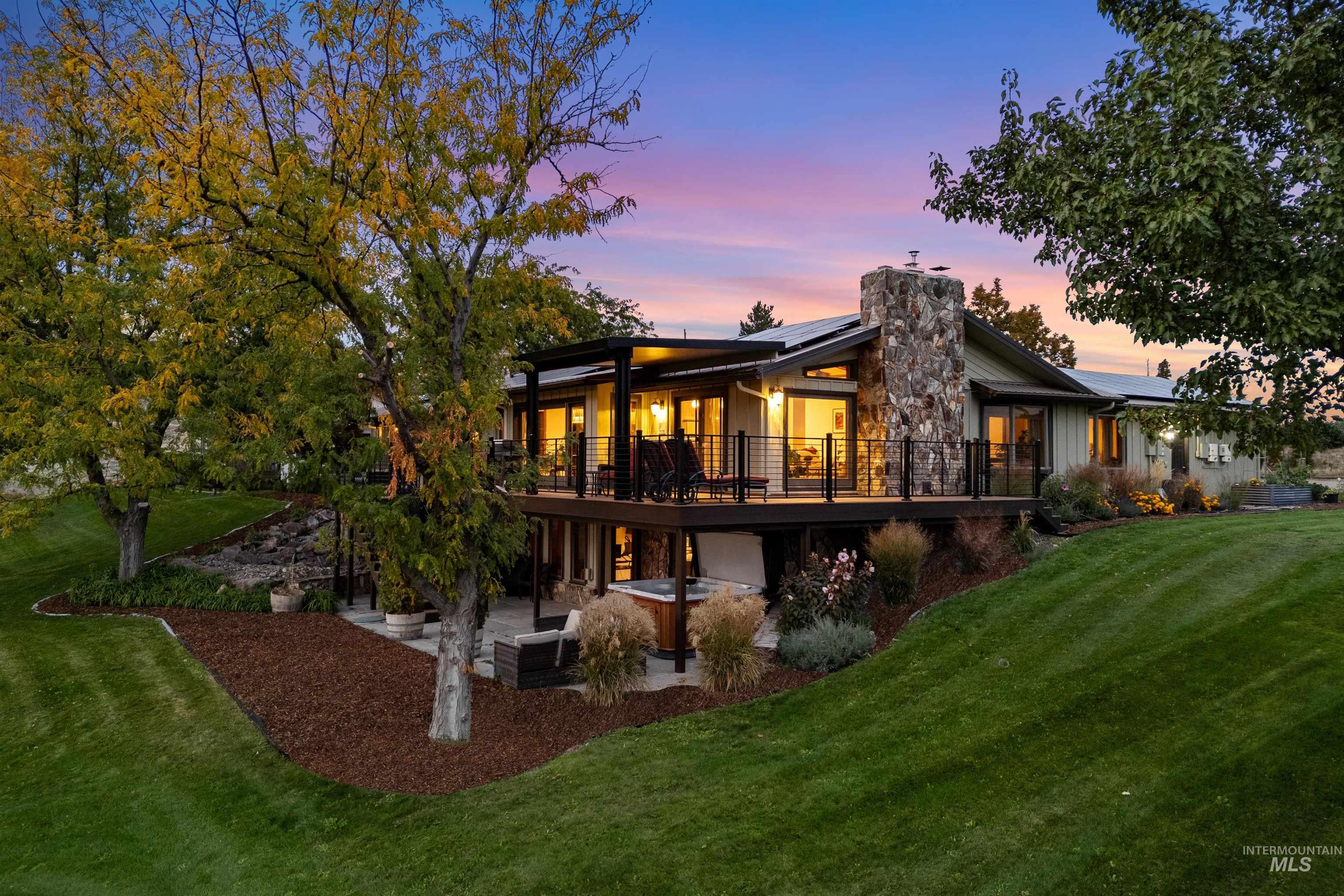 Back of house at dusk with a lawn, a chimney, solar panels, a patio, and a balcony