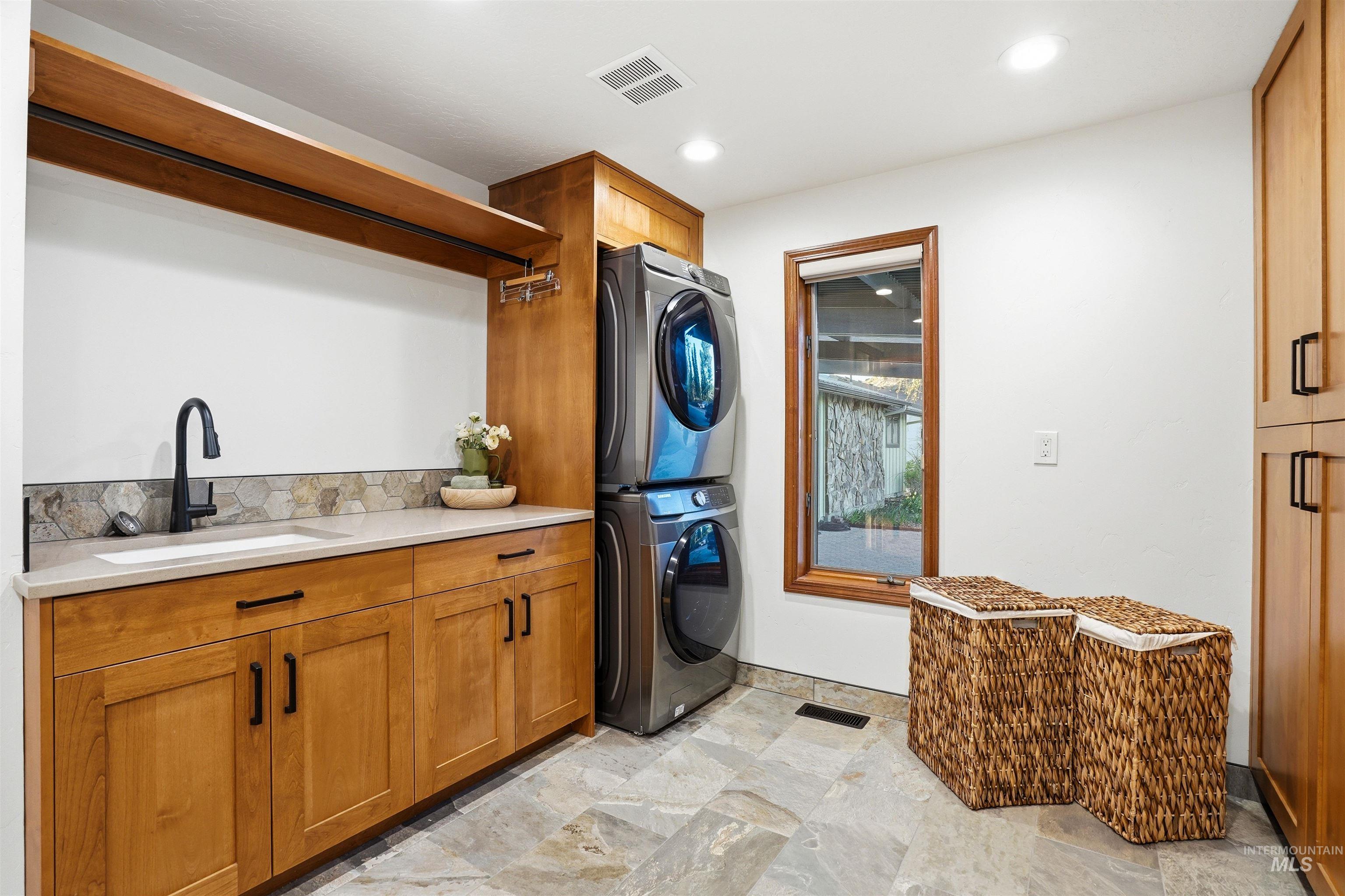 Laundry room with cabinet space, stacked washer and dryer, light stone finish floors, and recessed lighting