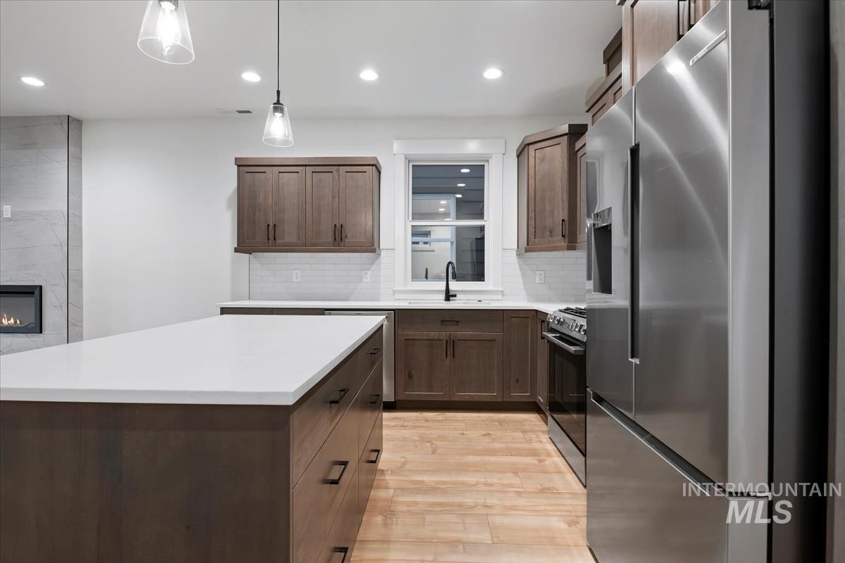 Kitchen with appliances with stainless steel finishes, hanging light fixtures, light wood-style floors, backsplash, and a center island