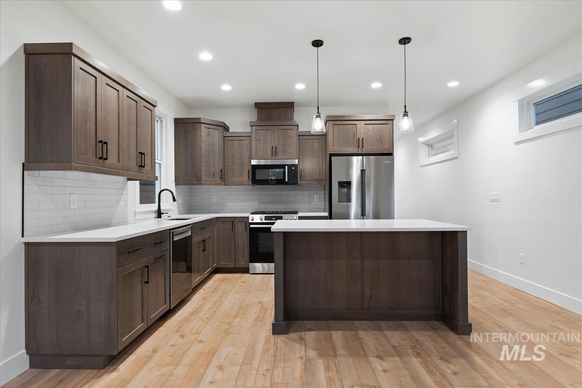Kitchen featuring tasteful backsplash, stainless steel appliances, dark brown cabinets, decorative light fixtures, and a center island
