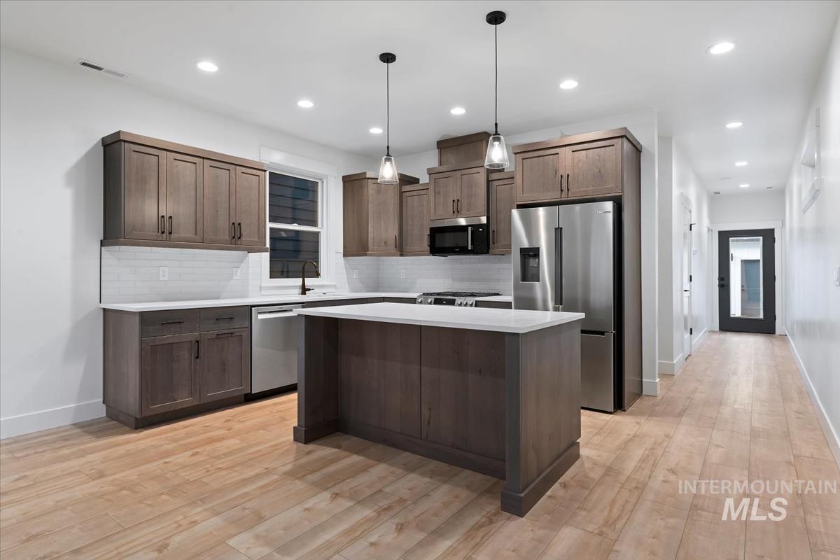 Kitchen featuring decorative light fixtures, tasteful backsplash, stainless steel appliances, a kitchen island, and recessed lighting