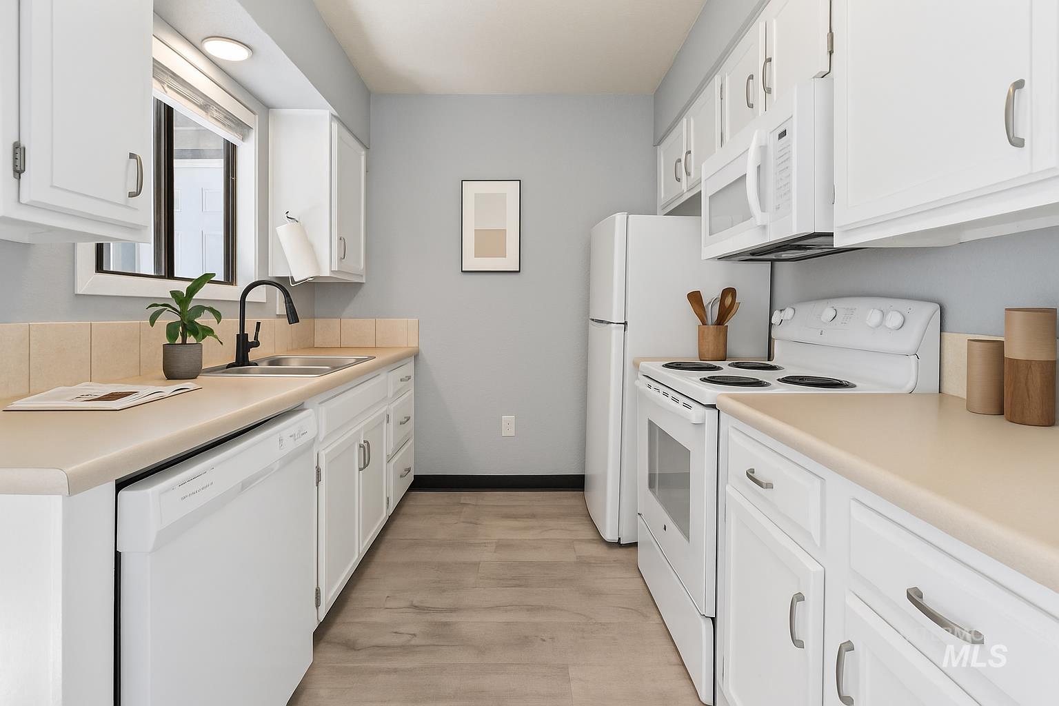 Kitchen with white appliances, white cabinets, light countertops, and light wood-style floors