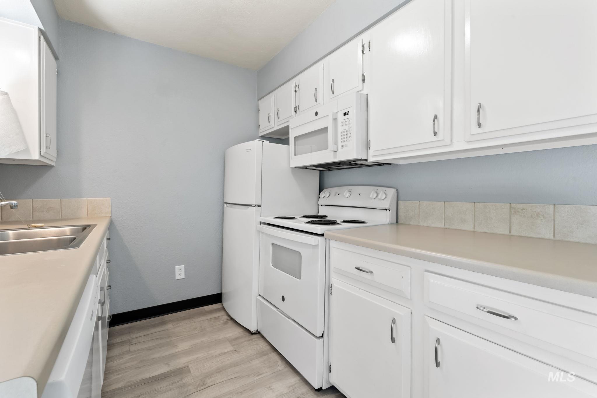 Kitchen featuring white appliances, white cabinets, light countertops, and light wood finished floors