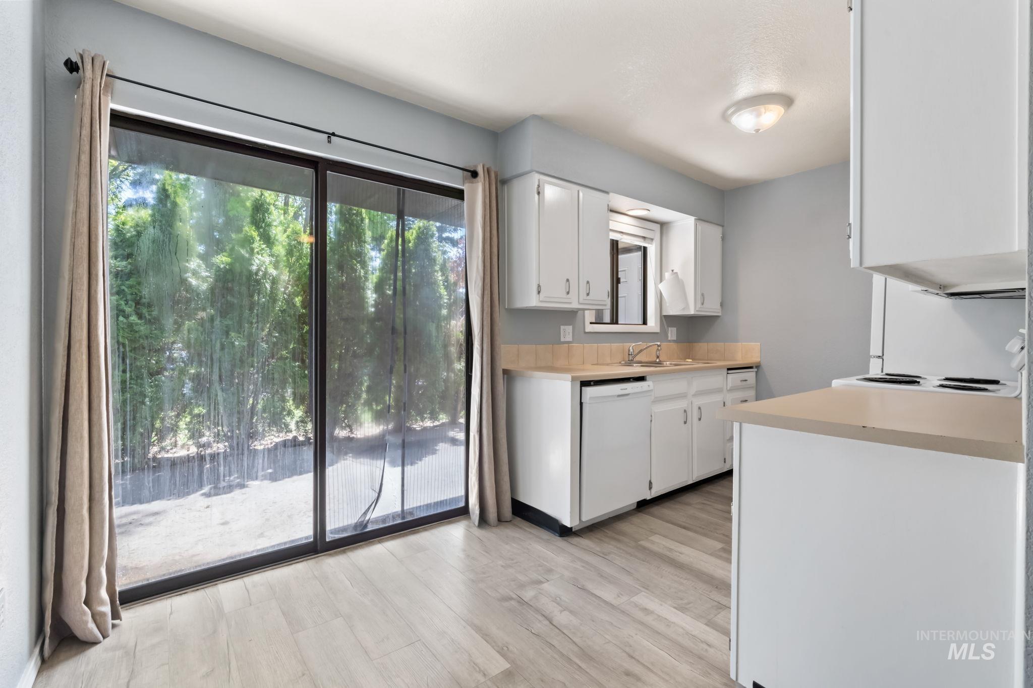Kitchen with light countertops, white cabinets, white appliances, and light wood-type flooring