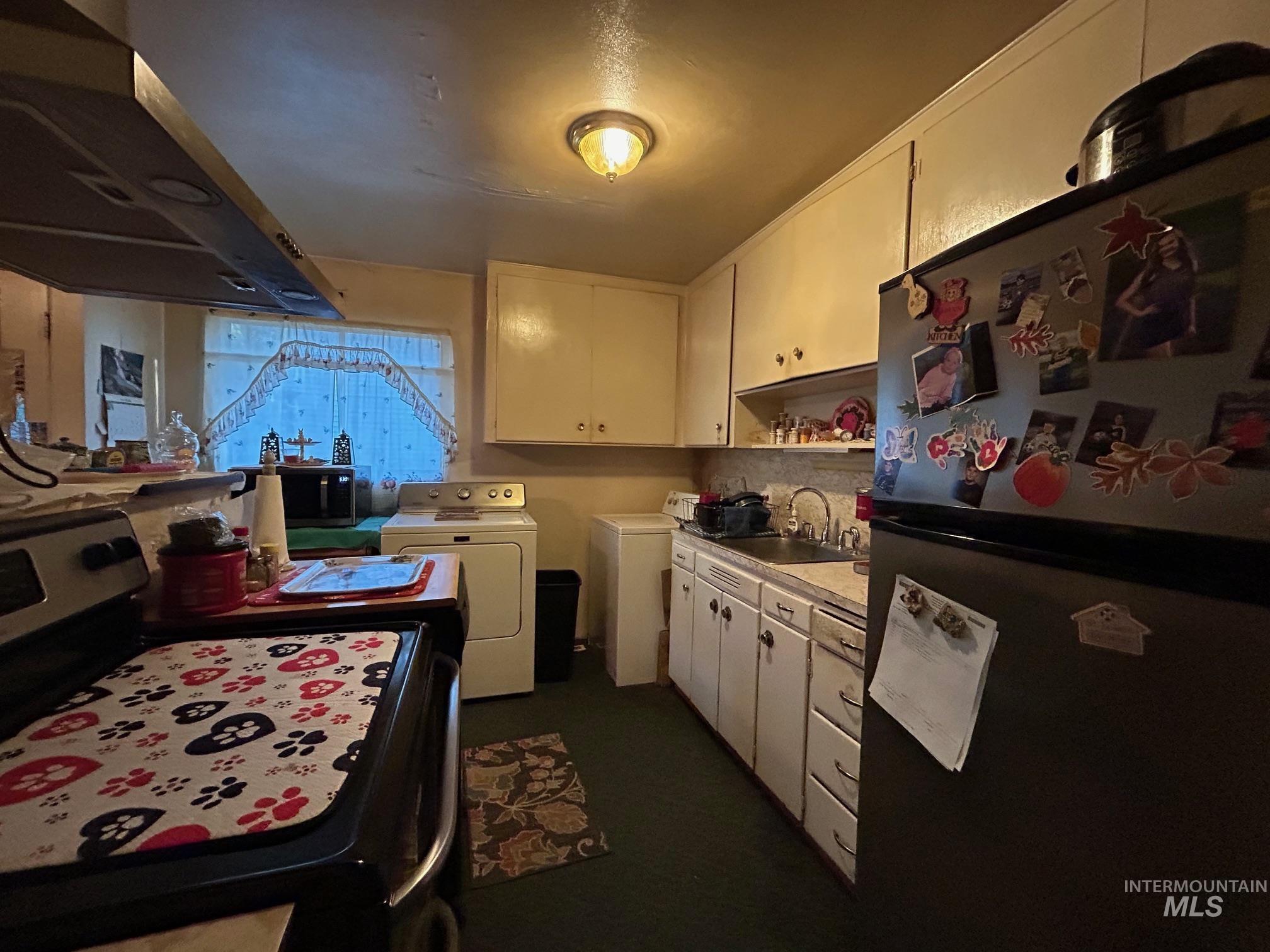 Kitchen with freestanding refrigerator, stainless steel electric stove, white cabinetry, light countertops, and washing machine and clothes dryer