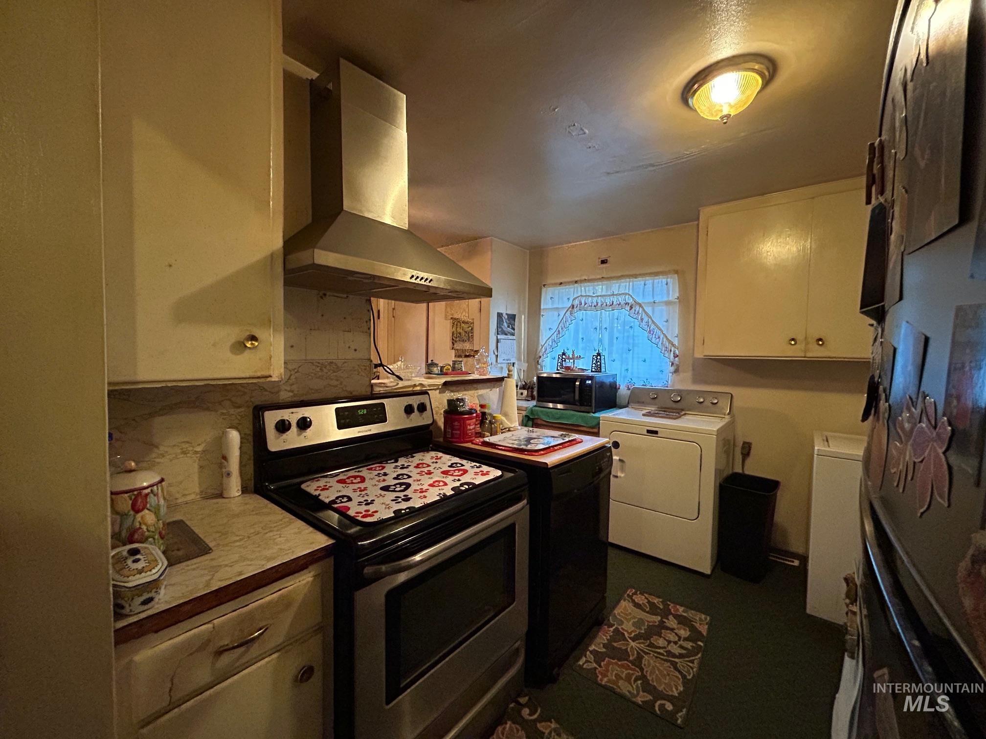Kitchen featuring stainless steel appliances, ventilation hood, light countertops, white cabinetry, and washer / dryer