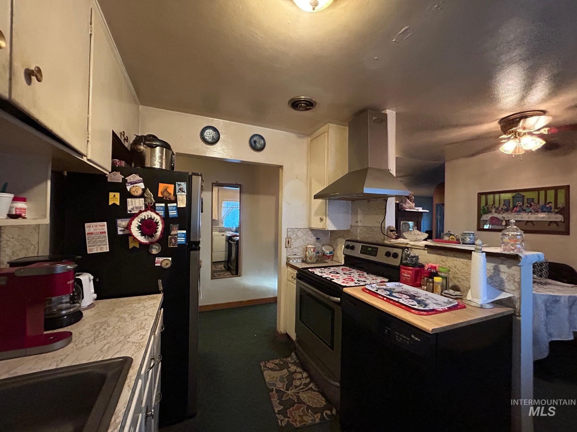 Kitchen with appliances with stainless steel finishes, range hood, light countertops, backsplash, and white cabinets