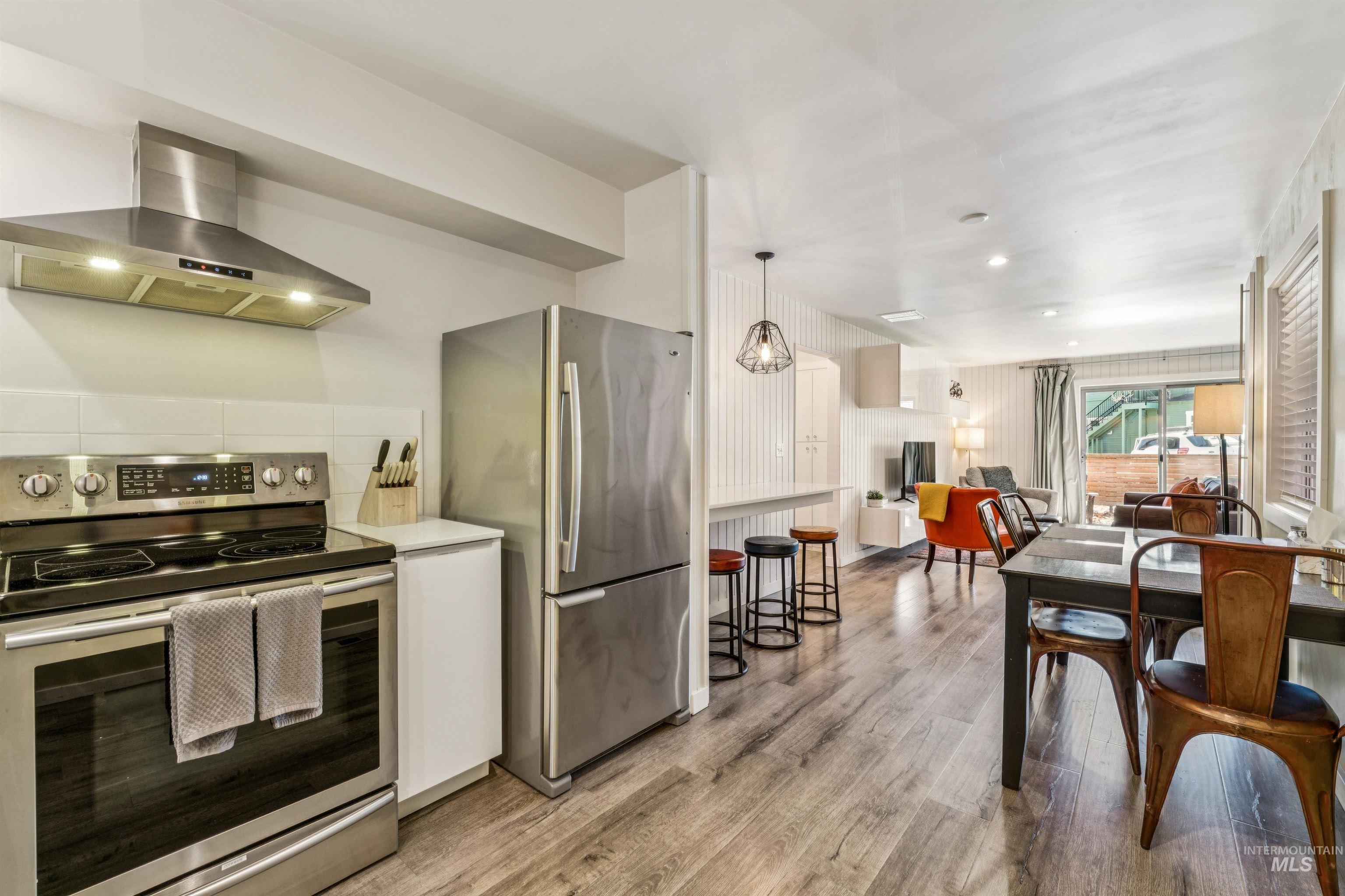 Kitchen with stainless steel appliances, ventilation hood, light wood finished floors, open floor plan, and white cabinetry