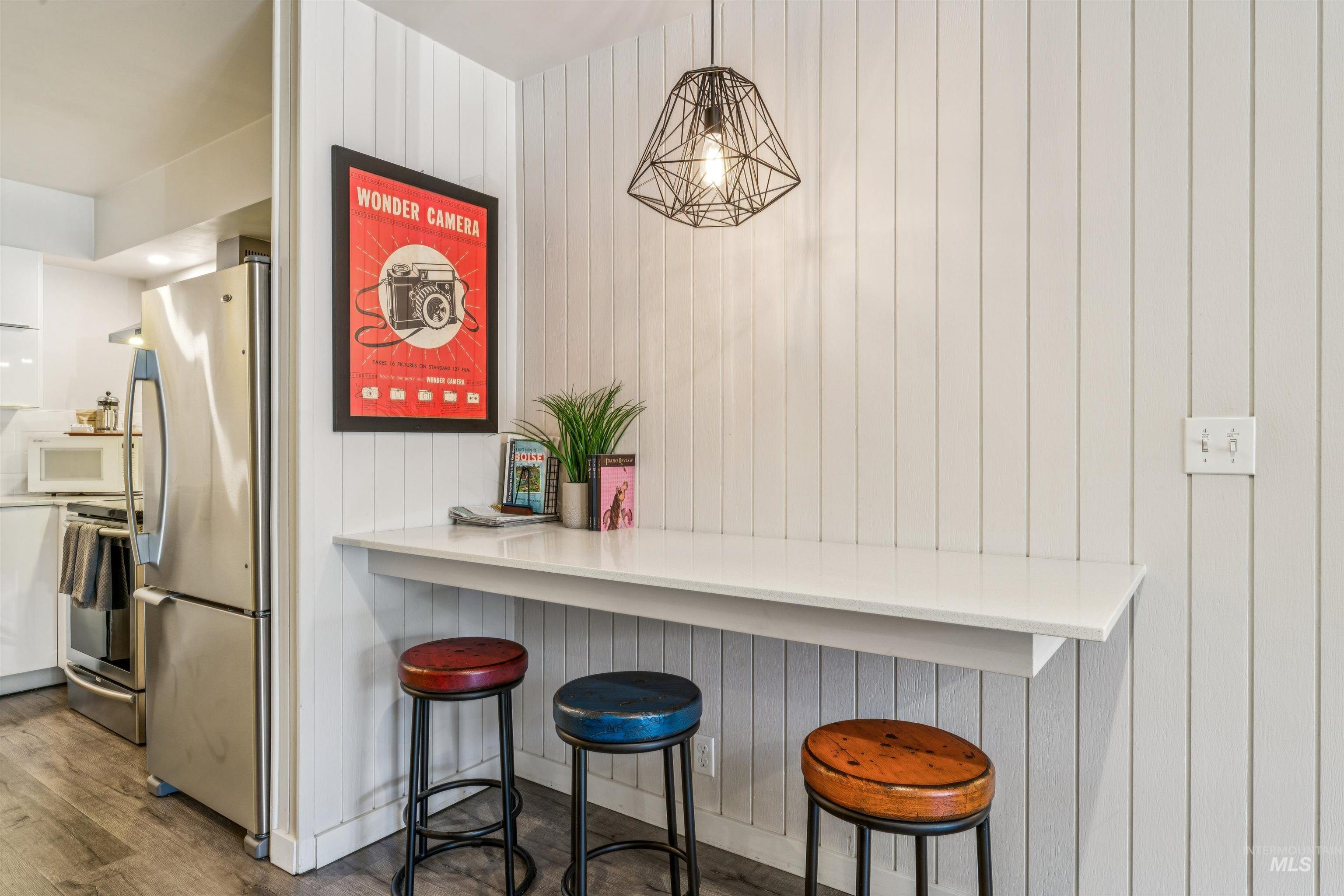Kitchen featuring a kitchen bar, stainless steel appliances, dark wood-style floors, hanging light fixtures, and light countertops