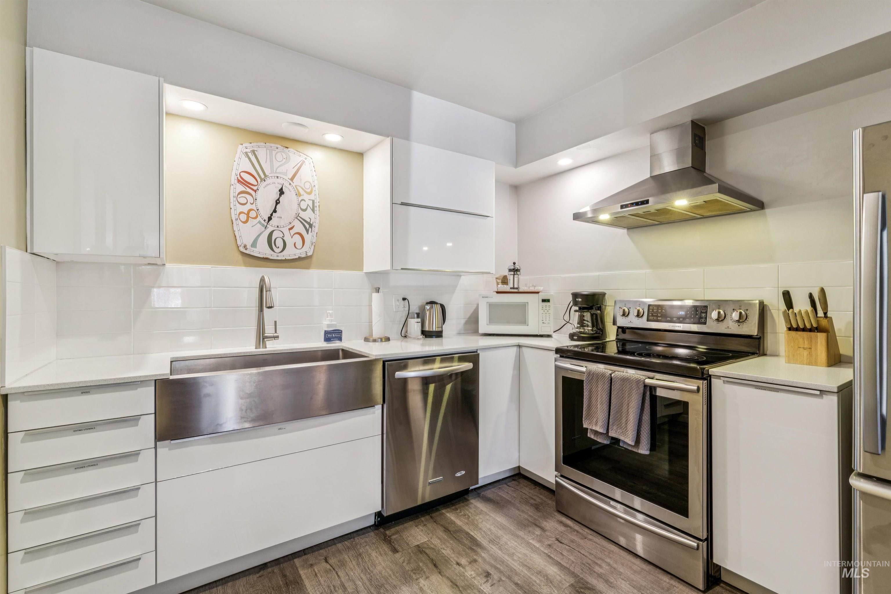 Kitchen with stainless steel appliances, extractor fan, white cabinetry, decorative backsplash, and dark wood-type flooring
