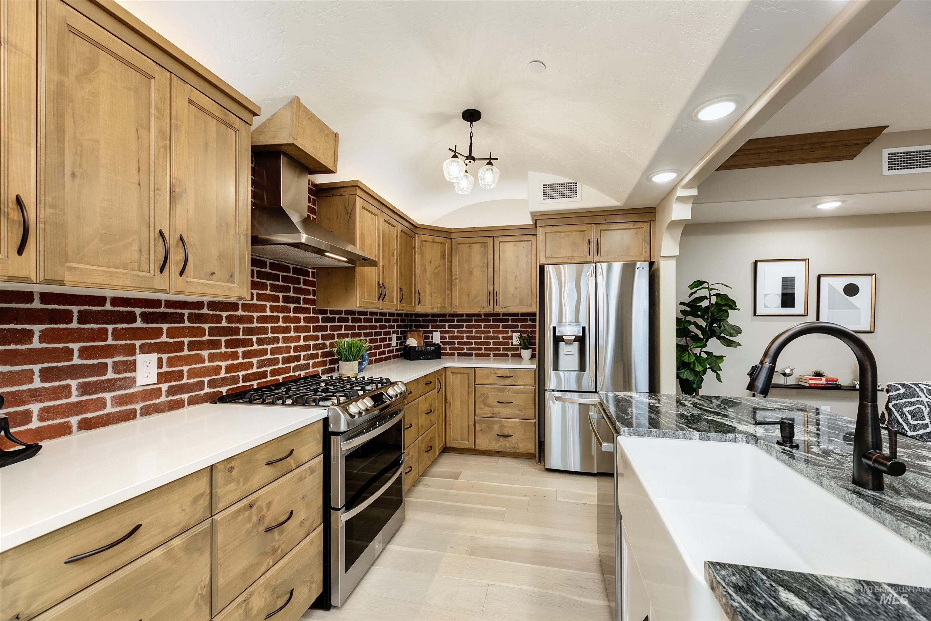 Kitchen with stainless steel appliances, light stone counters, a barrel ceiling, hanging light fixtures, and wood finish cabinetry