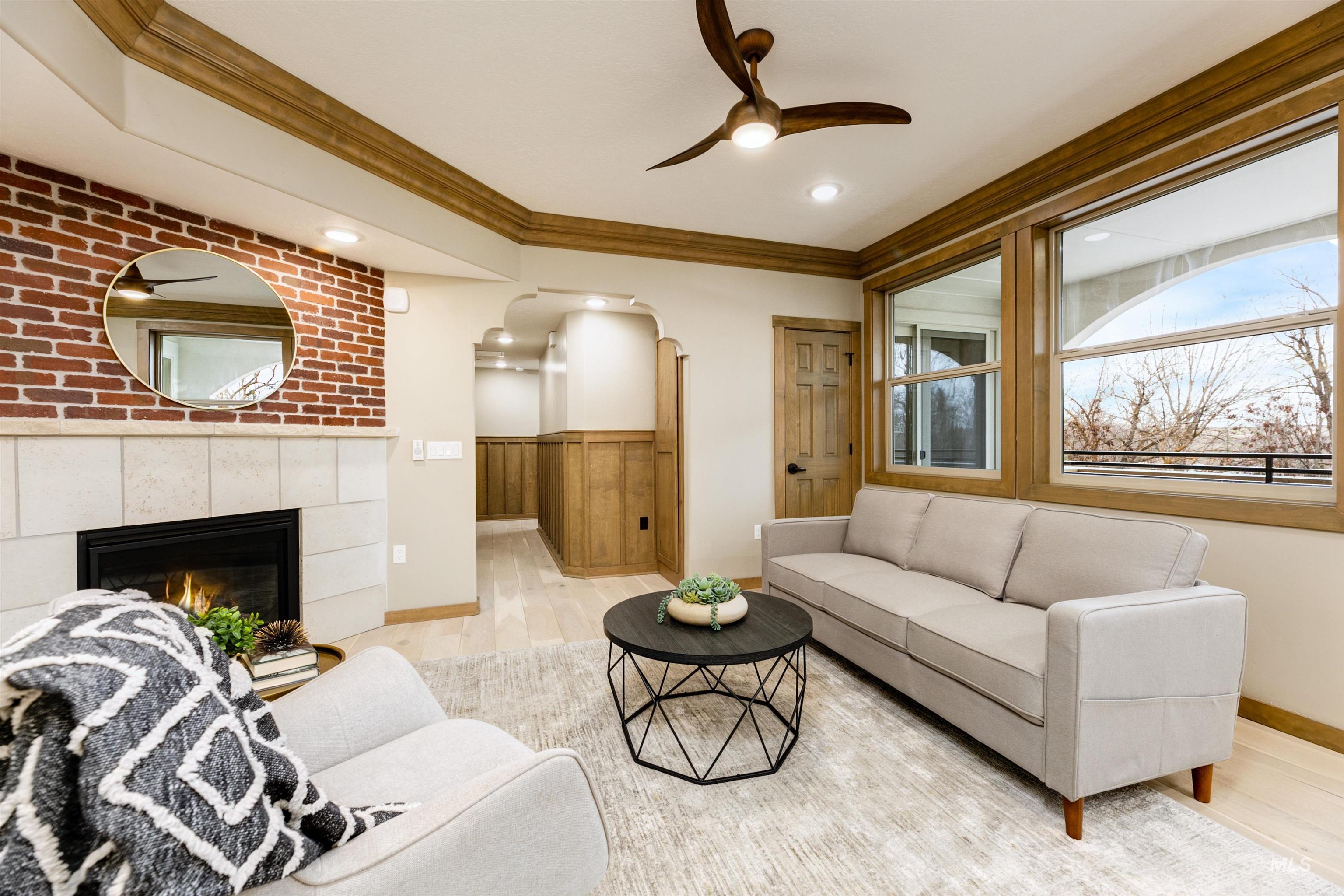 Living room with crown molding, a ceiling fan, light wood-style floors, arched walkways, and a tile fireplace