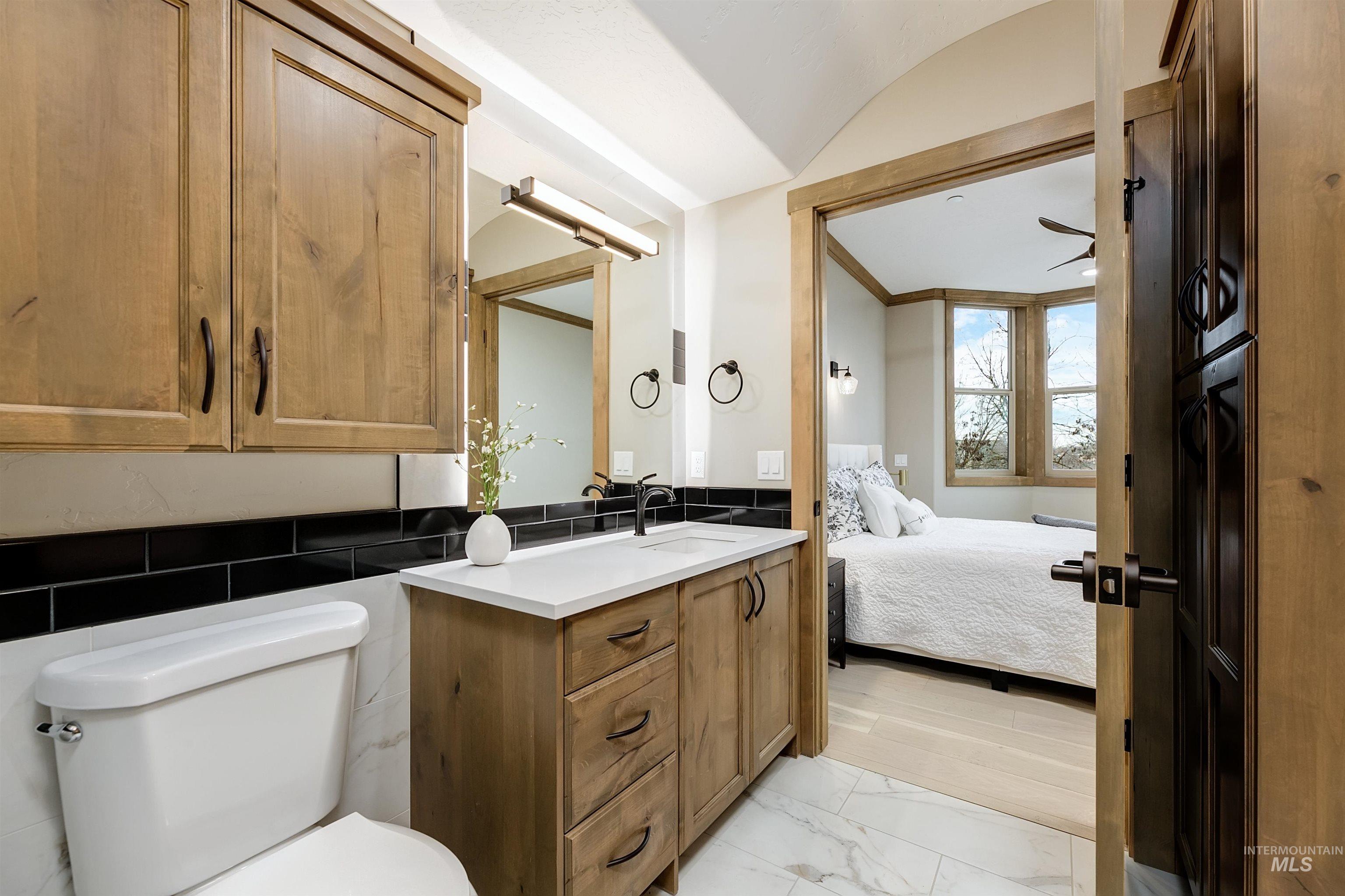 Ensuite bathroom featuring vanity, vaulted ceiling, light marble finish floors, a ceiling fan, and tile walls