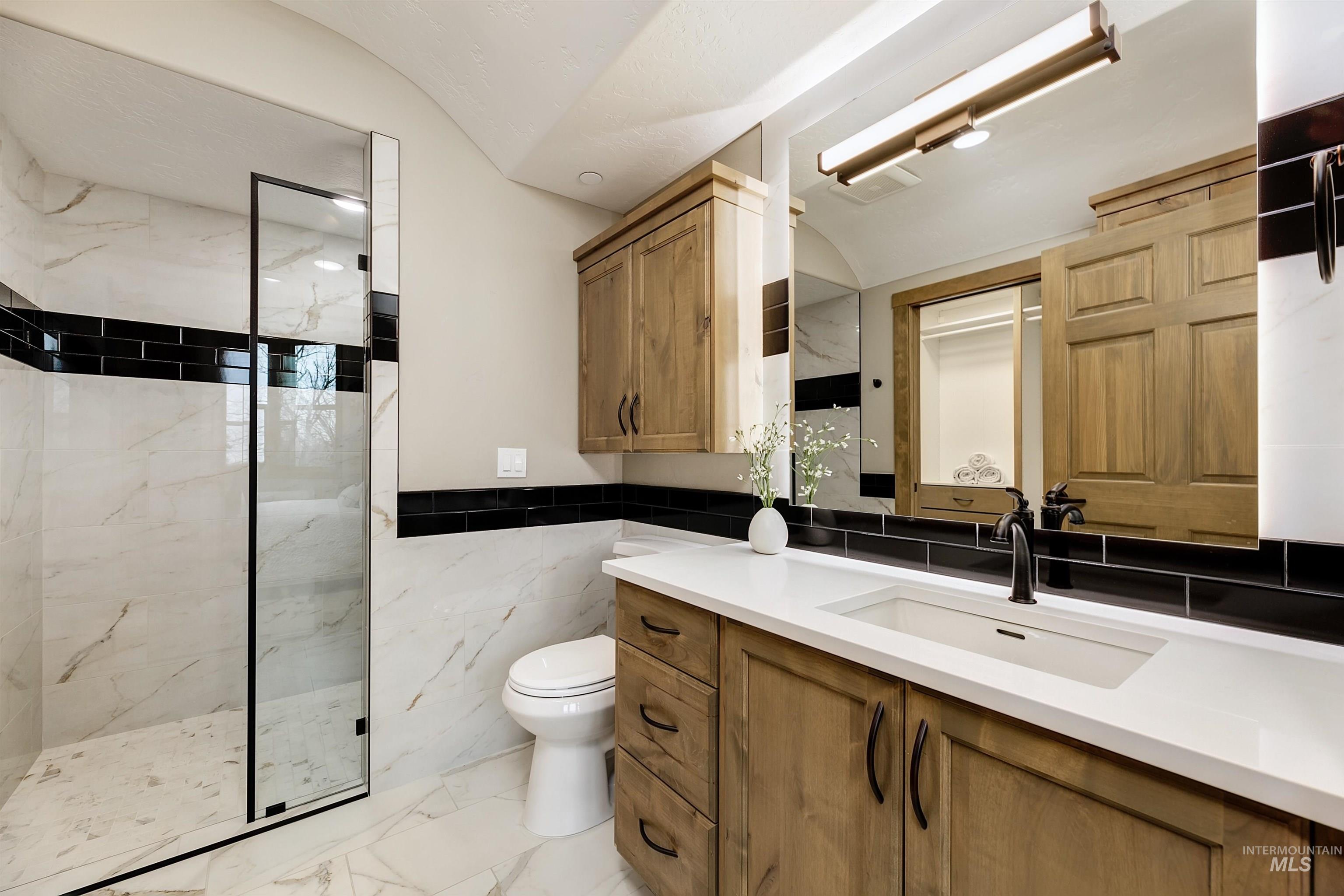 Full bathroom with a marble finish shower, vanity, tile walls, and light marble finish flooring