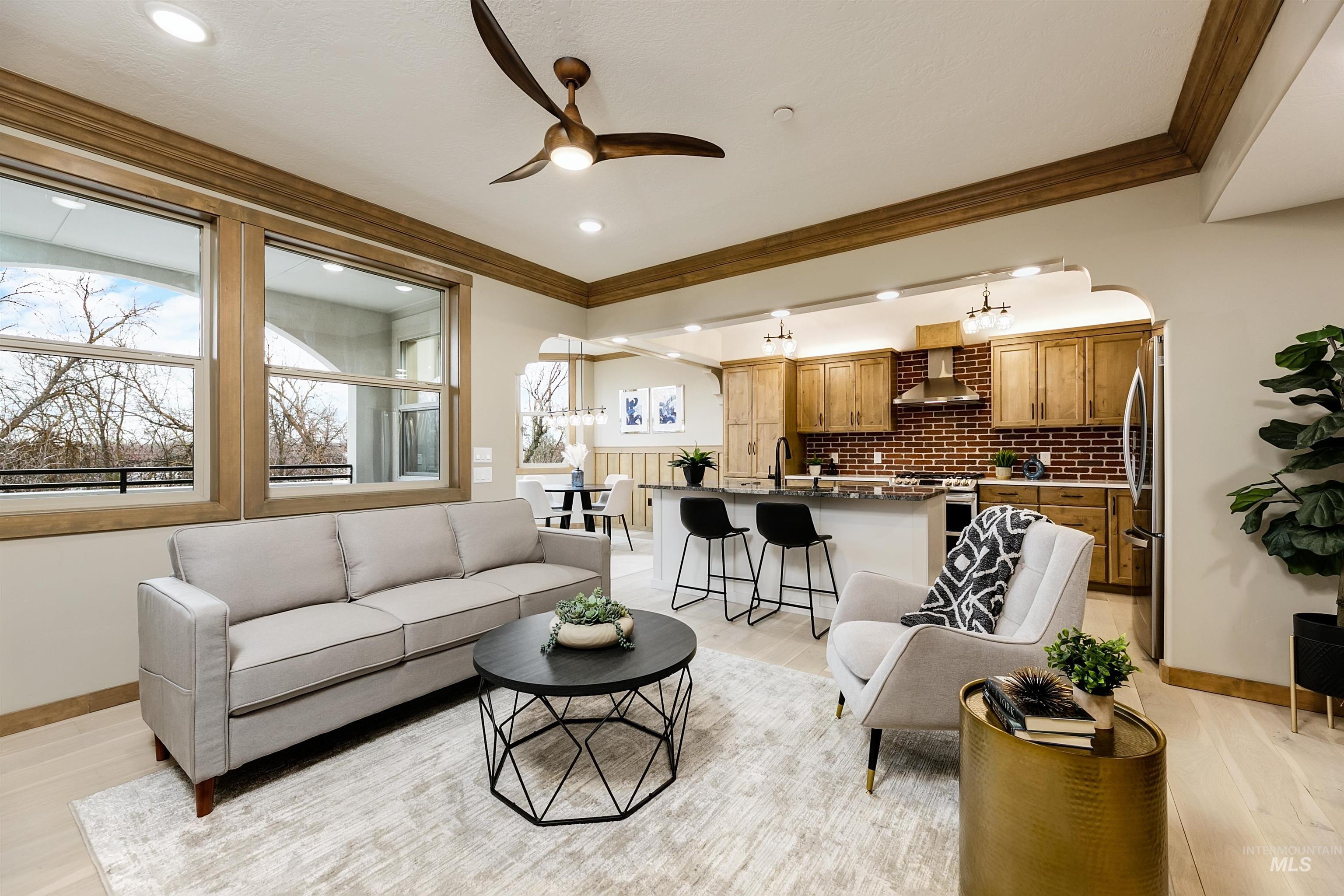 Living area with arched walkways, ceiling fan, light wood finished floors, and crown molding