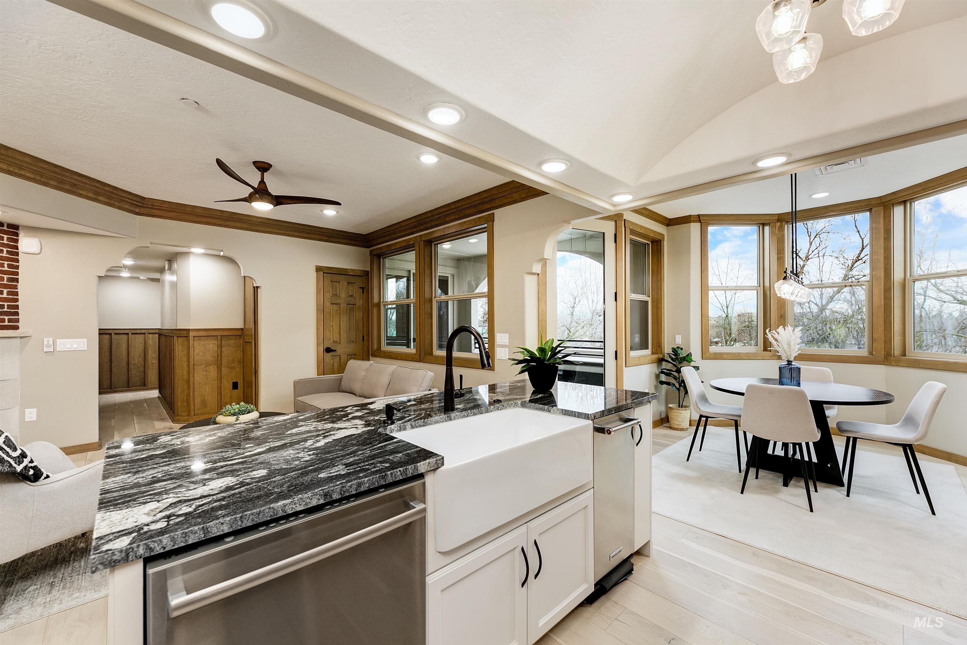 Kitchen with stainless steel dishwasher, arched walkways, a center island with sink, light wood-style flooring, and a ceiling fan