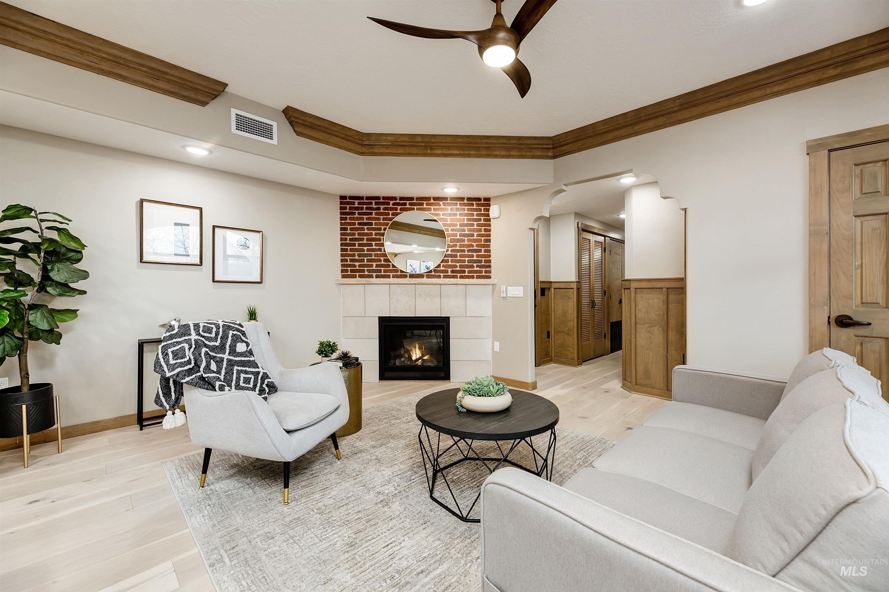 Living area with light wood-style floors, ceiling fan, crown molding, a fireplace, and arched walkways