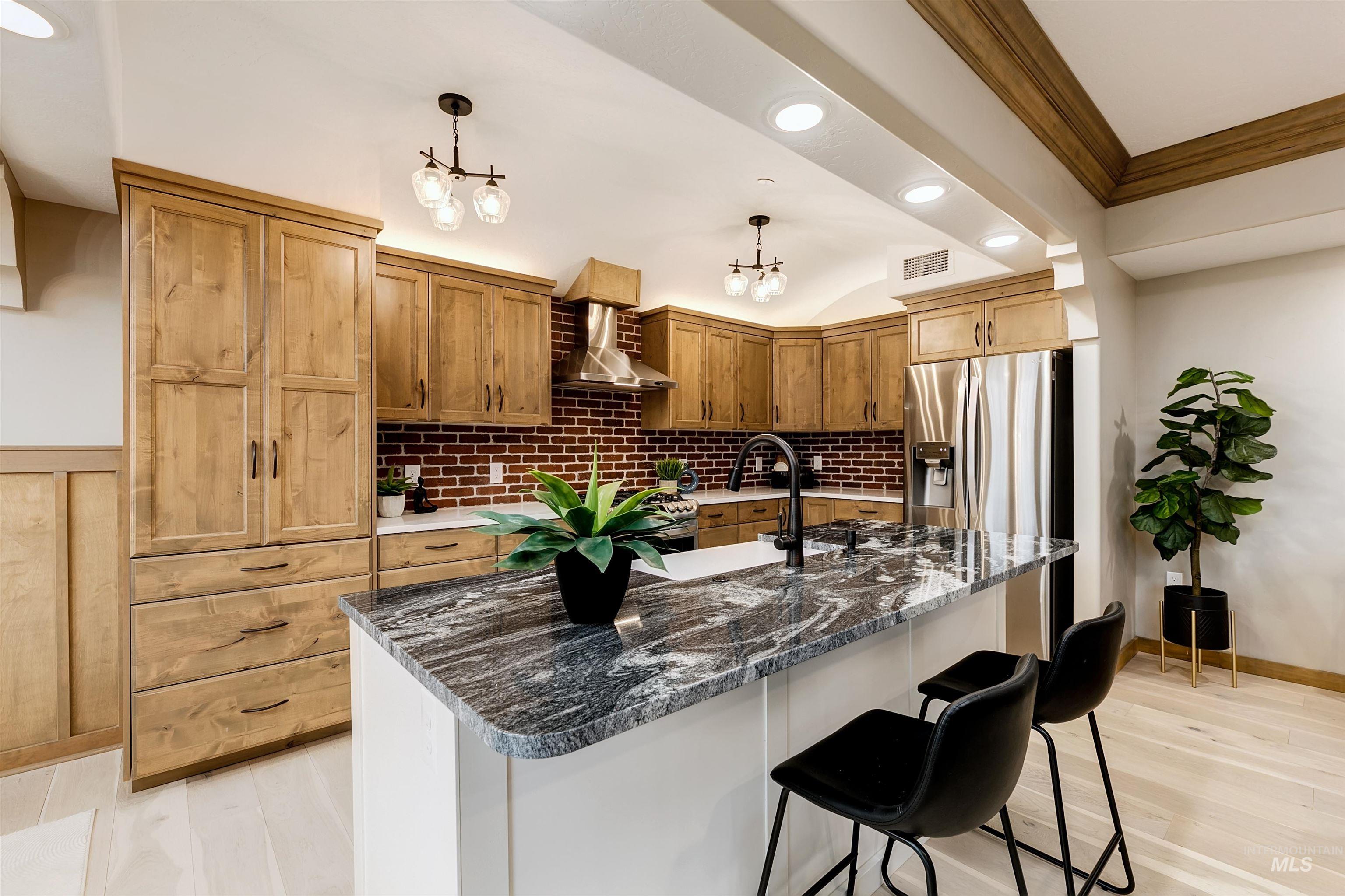 Kitchen featuring a kitchen breakfast bar, crown molding, light wood finished floors, dark stone counters, and a center island with sink
