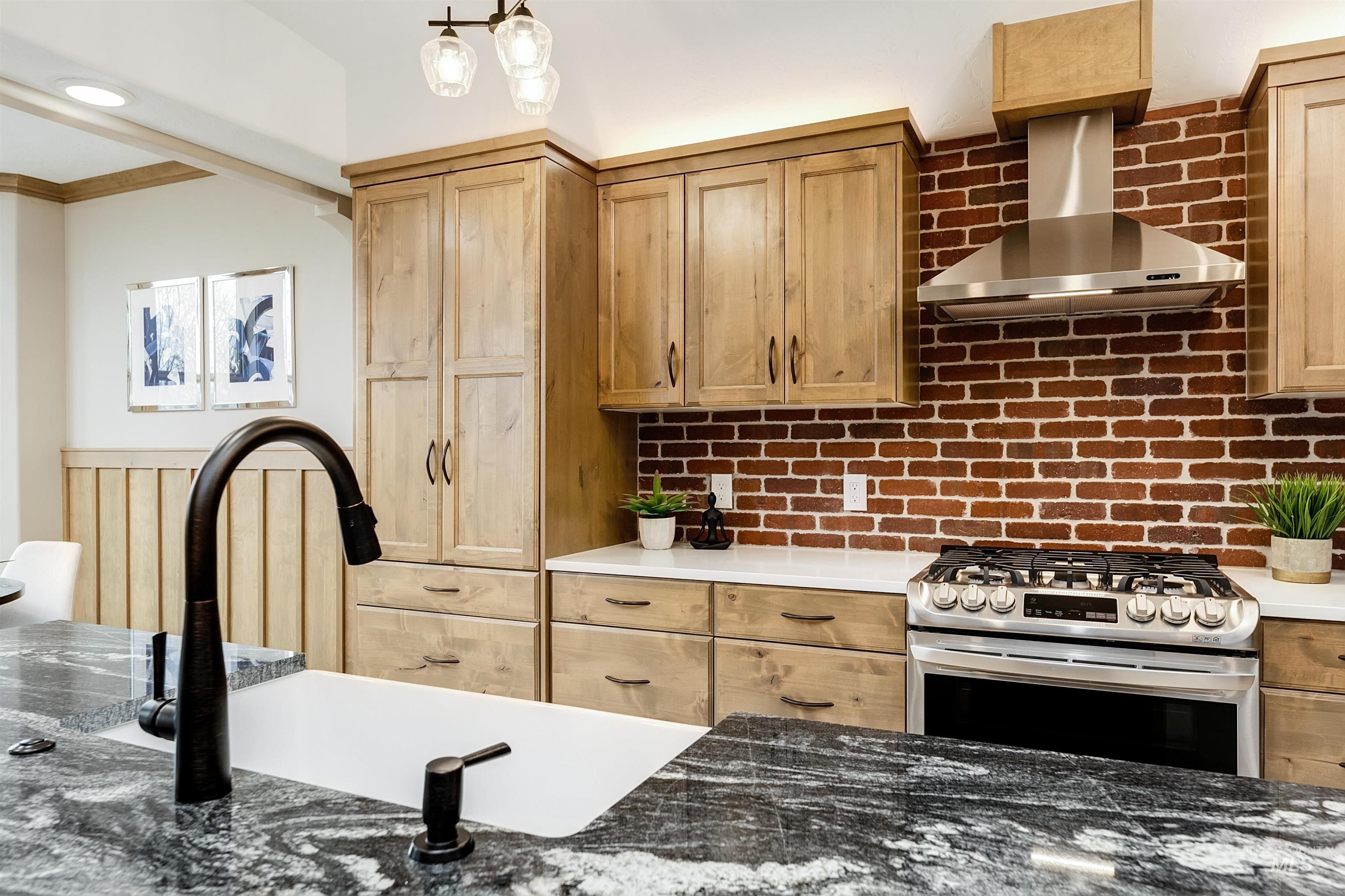 Kitchen featuring stainless steel gas stove, dark stone counters, crown molding, backsplash, and light wood finish cabinetry