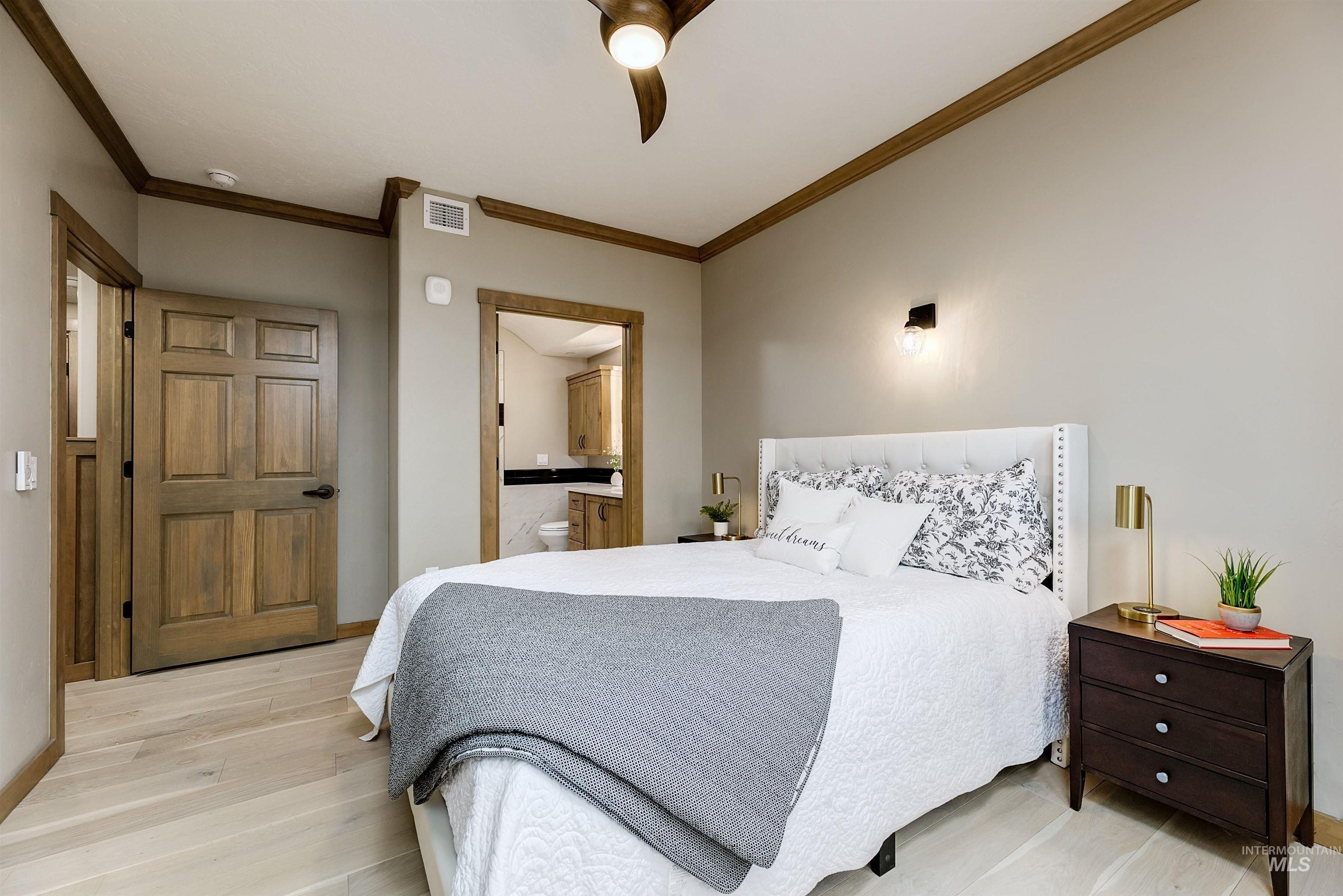 Bedroom featuring light wood-style floors, crown molding, a ceiling fan, and ensuite bathroom