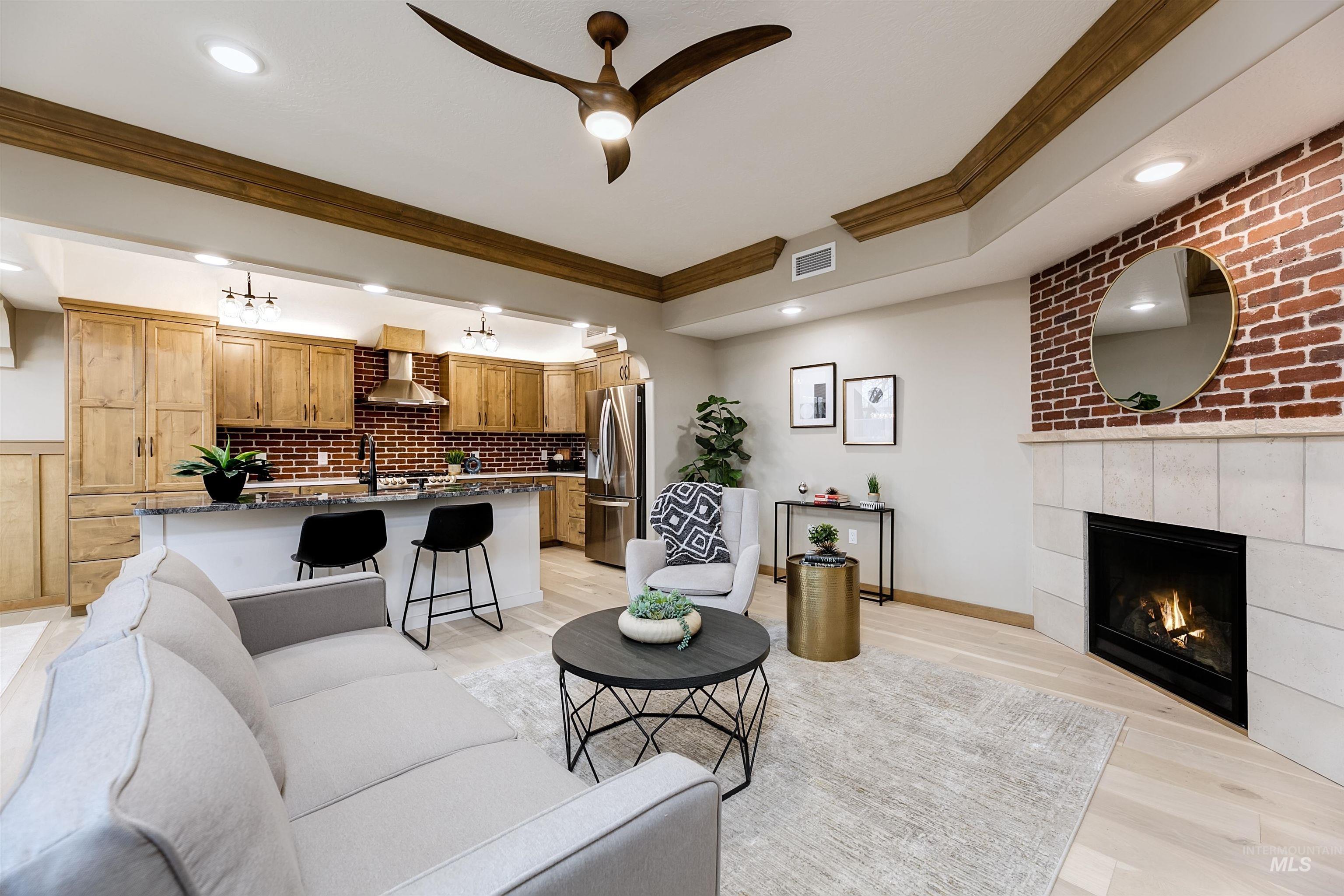 Living room with ceiling fan, ornamental molding, a tiled fireplace, and light wood-style flooring