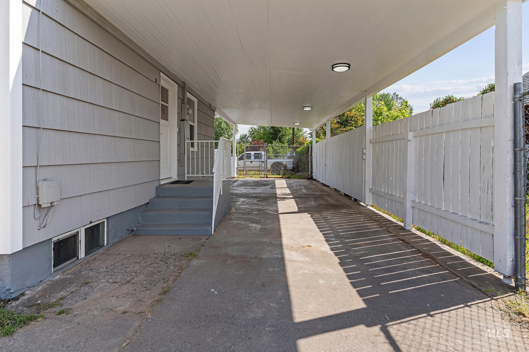 Covered carport with integrated lighting, providing sheltered access to the side entry