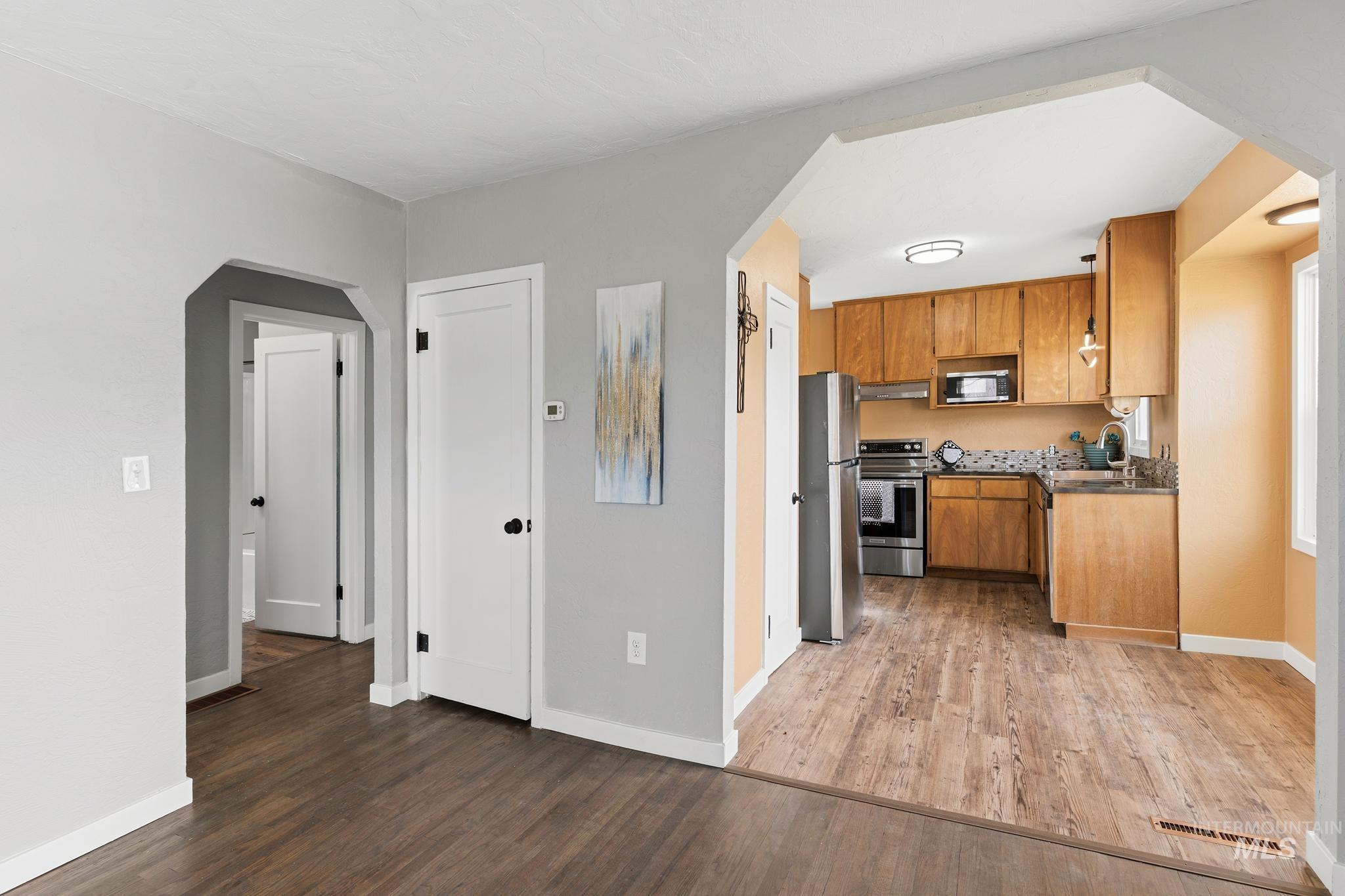 Kitchen with wood-finish flooring, natural wood cabinetry, stainless steel appliances, and a patterned tile backsplash