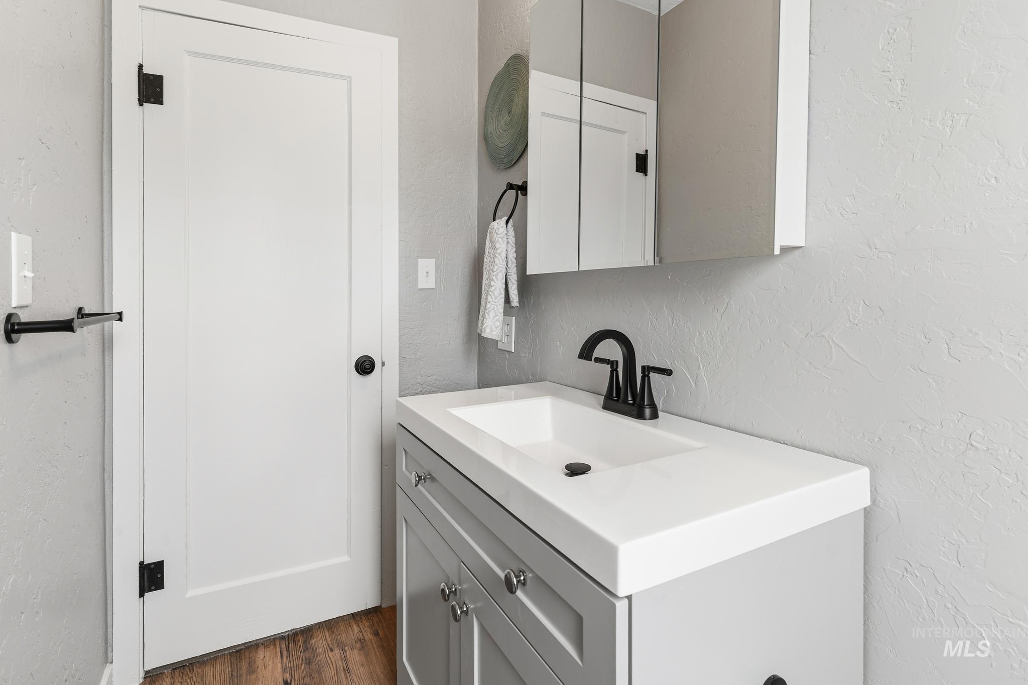 Contemporary vanity featuring a white integrated sink and countertop, matte black faucet, and a wall-mounted mirrored medicine cabinet