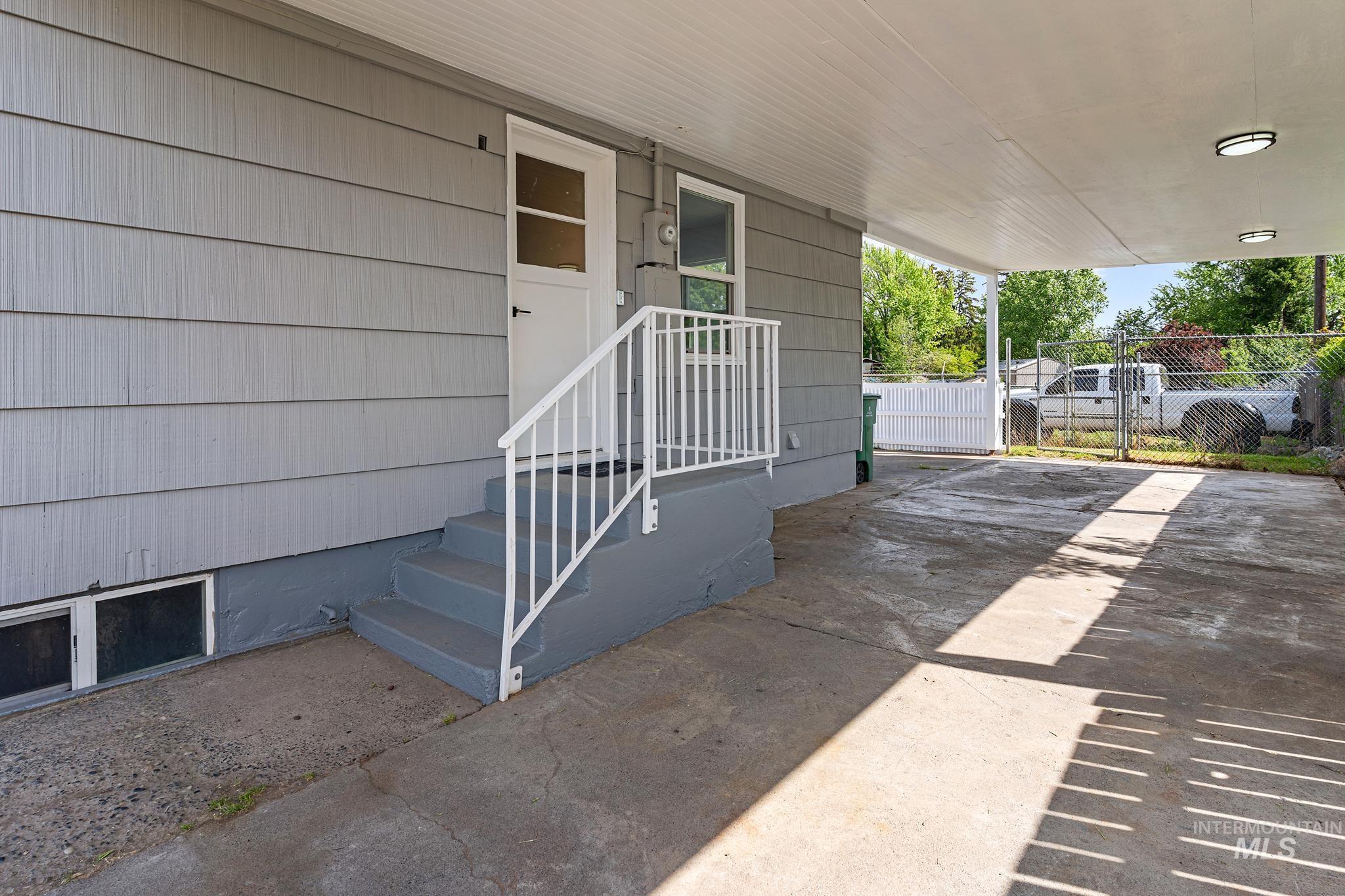 Covered carport featuring a concrete surface, overhead lighting, and direct entry to the property via an exterior door with a window