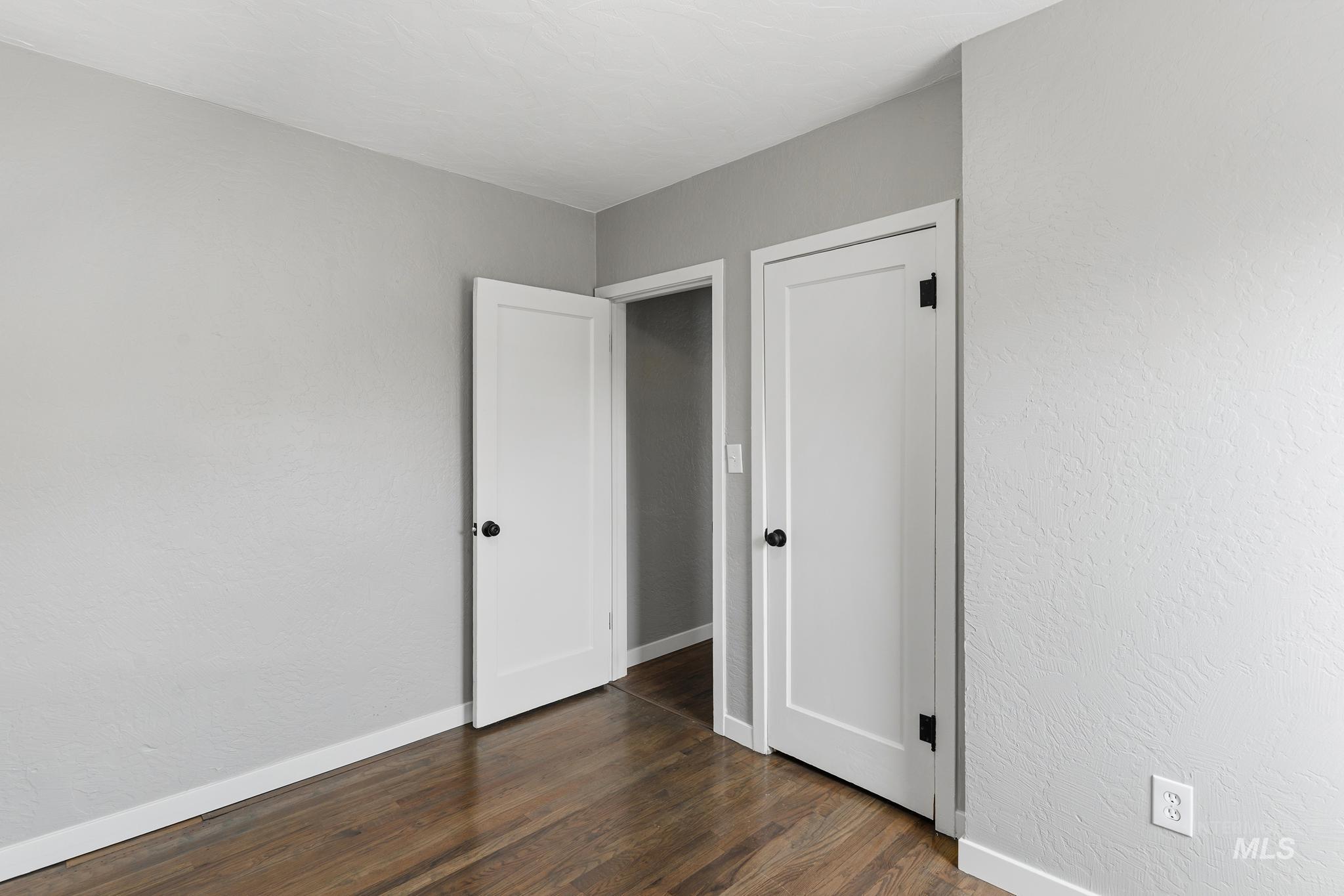 Interior room featuring wood-finish flooring, light grey painted walls, white baseboards, and two white panel doors with black hardware