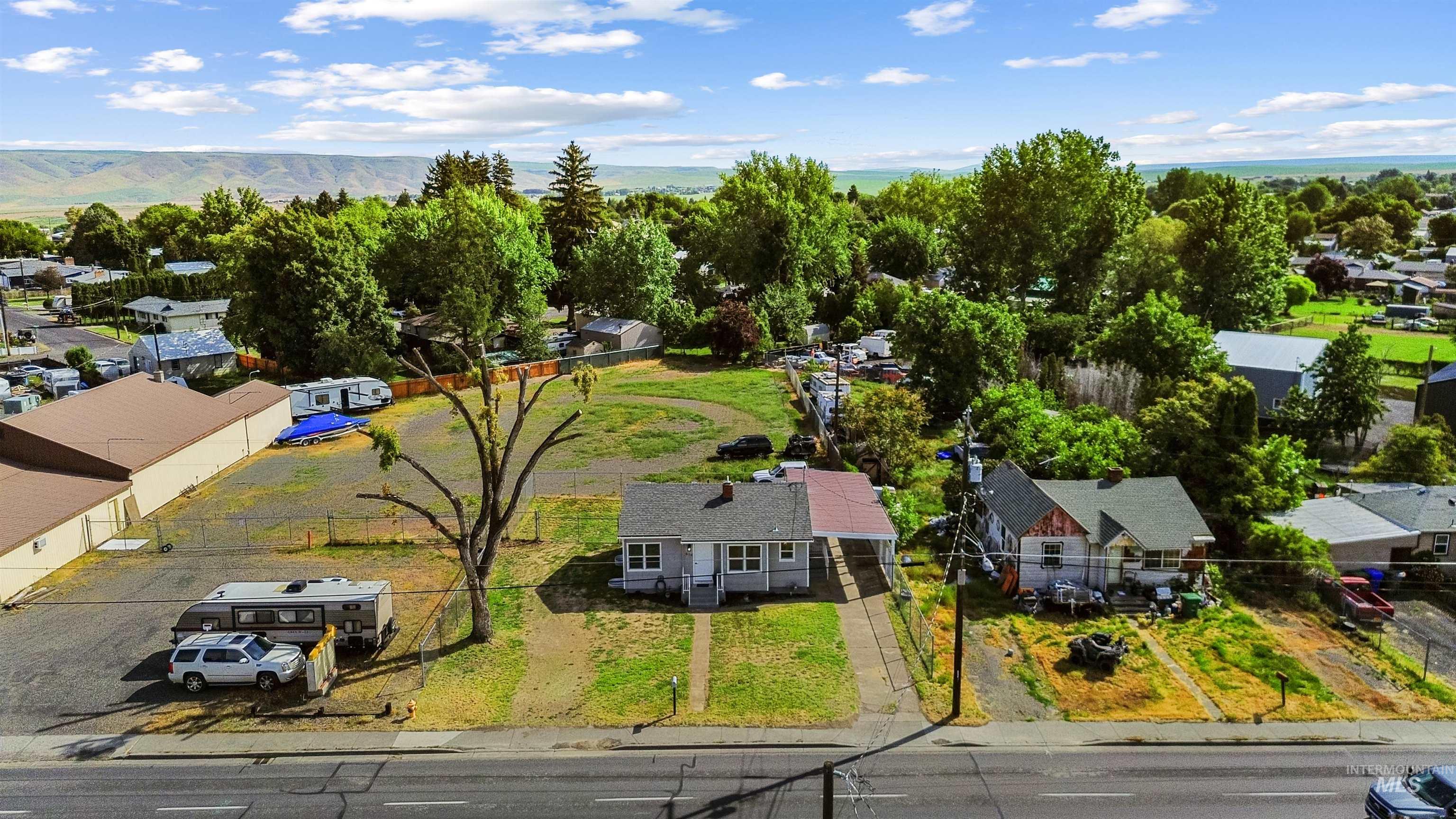 Expansive property lot featuring two single-story residences, a large undeveloped grassy area, and a paved commercial-style parking area with a fenced perimeter