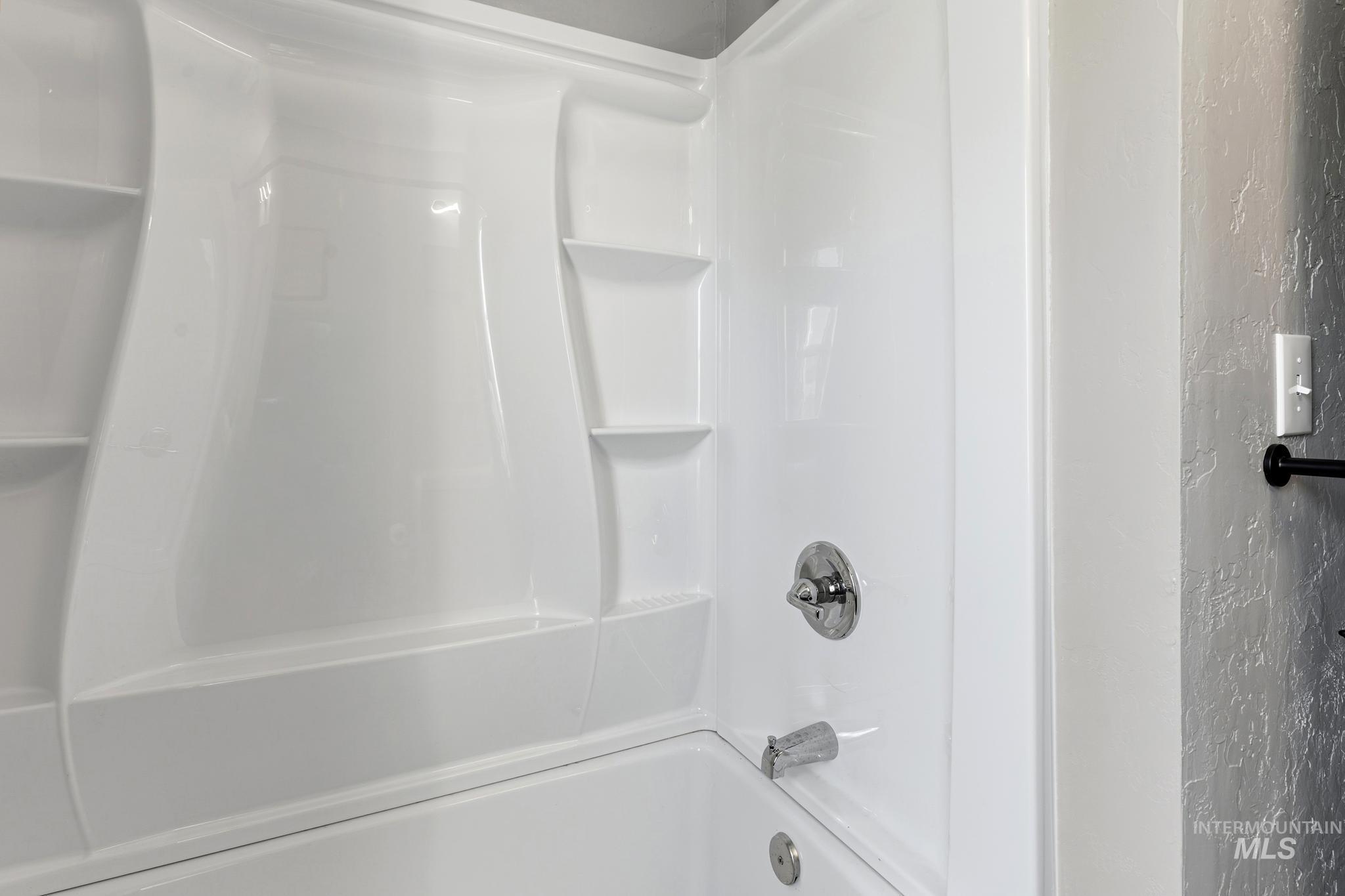 White fiberglass tub and shower combination featuring integrated shelving