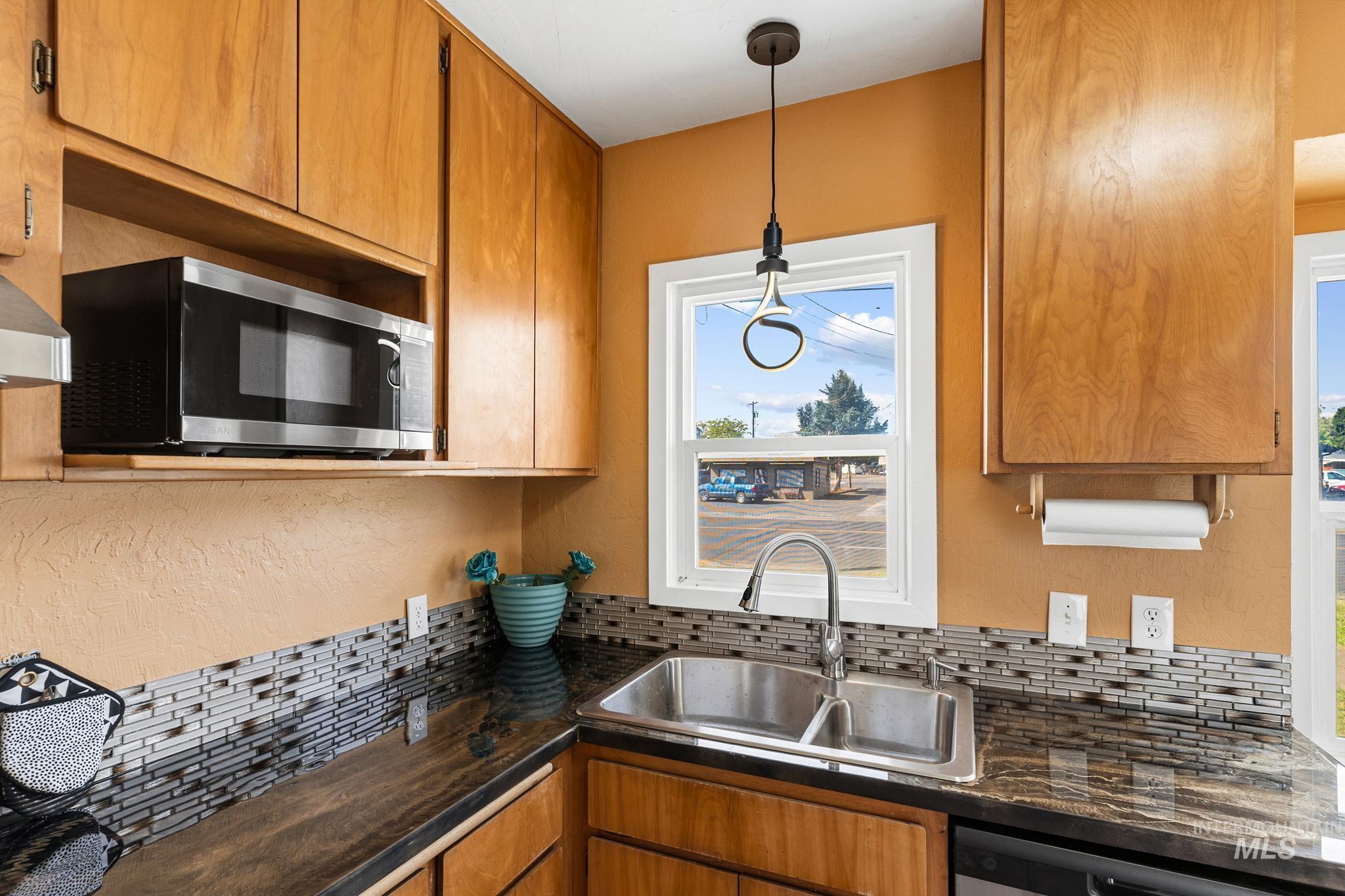 Kitchen featuring a double-basin stainless steel sink, dark granite countertops, and a mosaic tile backsplash