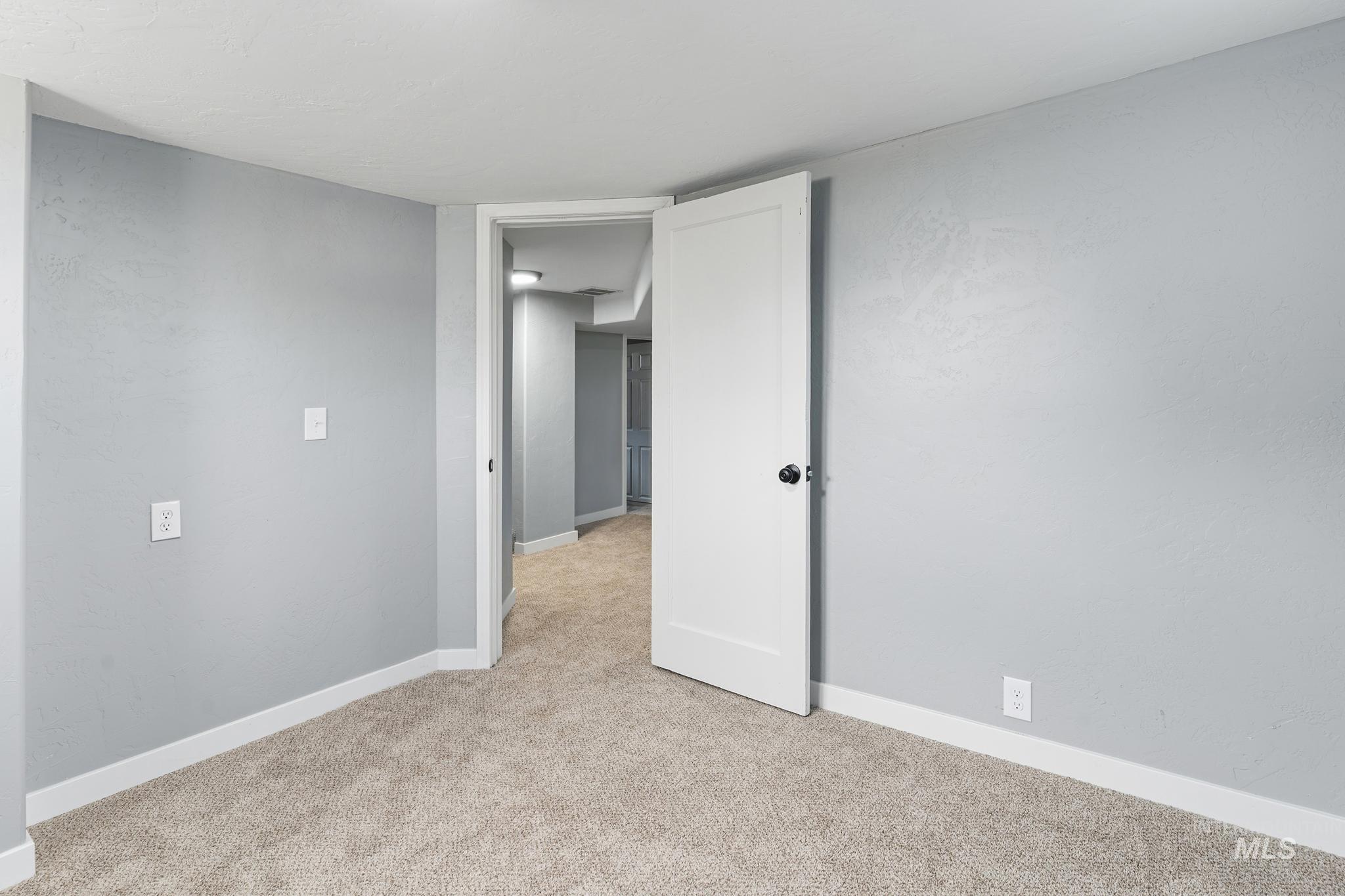 Spacious room featuring light gray walls, white trim, and neutral carpet flooring