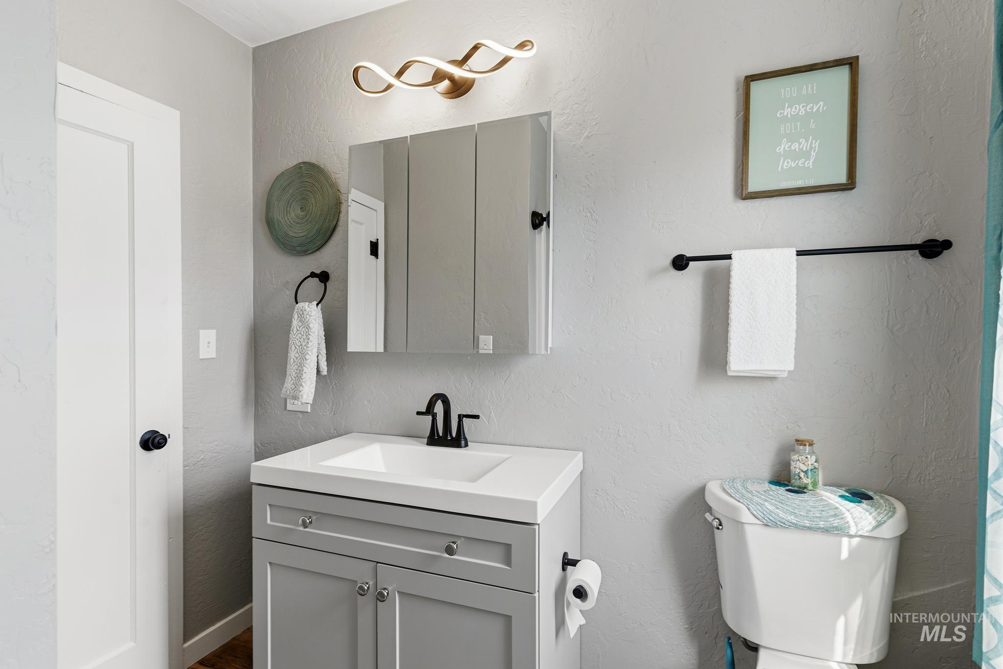 Bathroom featuring a light gray vanity with a single sink and matte black faucet, a mirrored medicine cabinet, and a decorative vanity light fixture