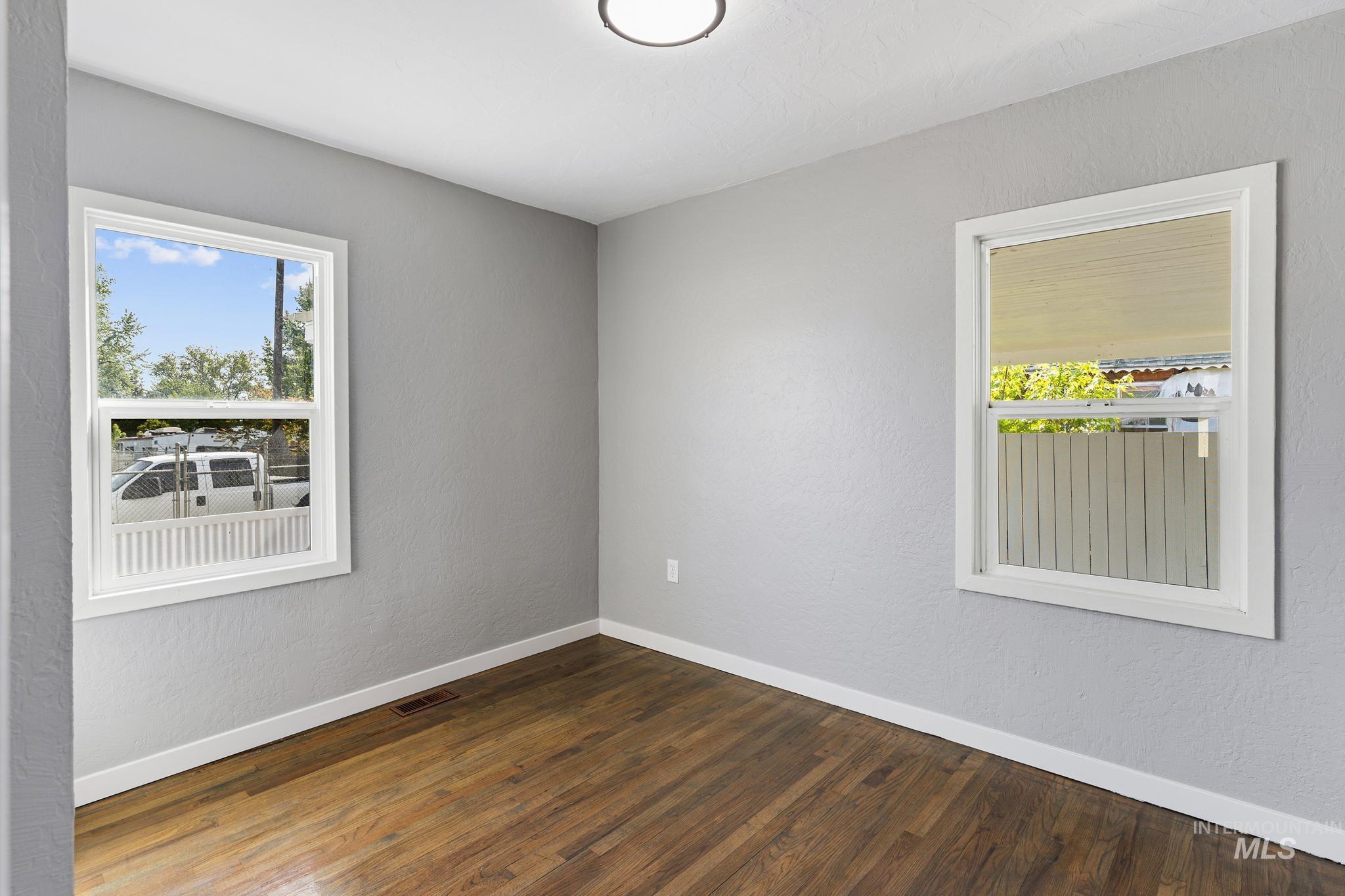 Room featuring two windows with white trim, wood-finish flooring, light gray walls, and white baseboards