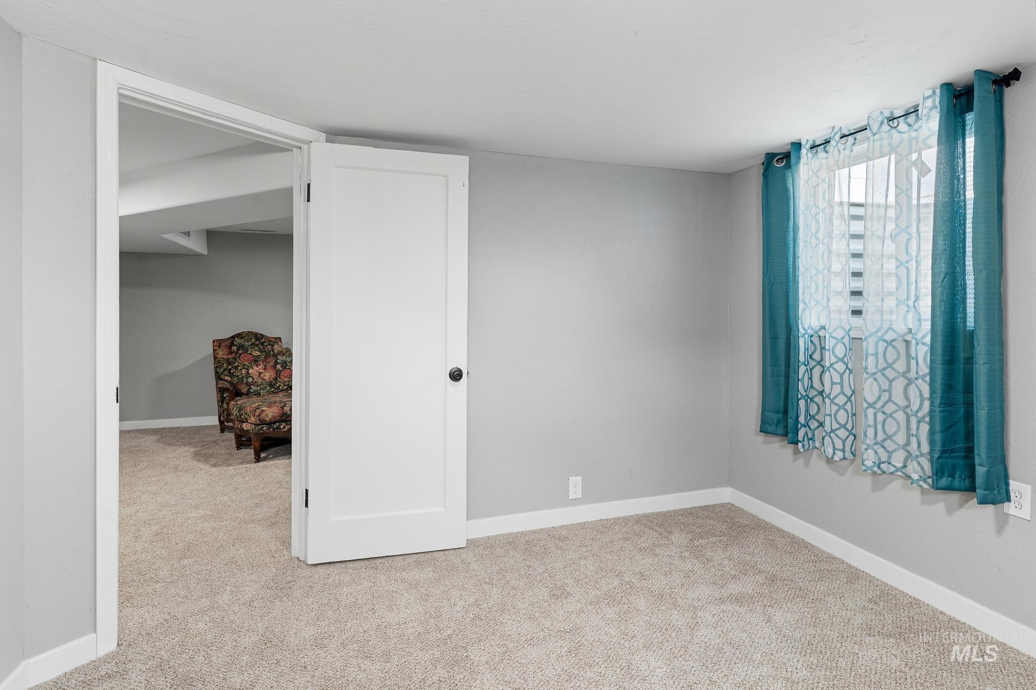 Interior room with light gray walls, light-colored carpet flooring, white baseboards, and a white interior door with a black knob