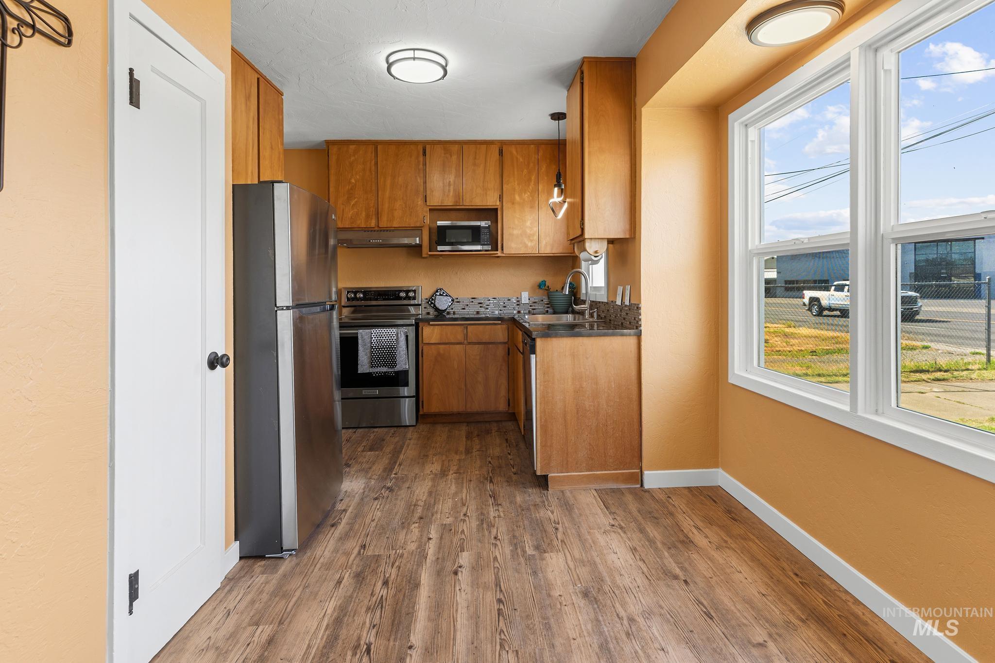 Kitchen featuring wood-finish flooring, light wood cabinetry, stainless steel appliances, and a tiled backsplash